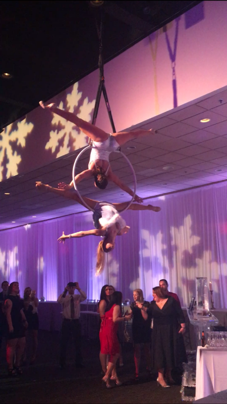 Aerial duo performing on a Lyra/Aerial Hoop in white costumes