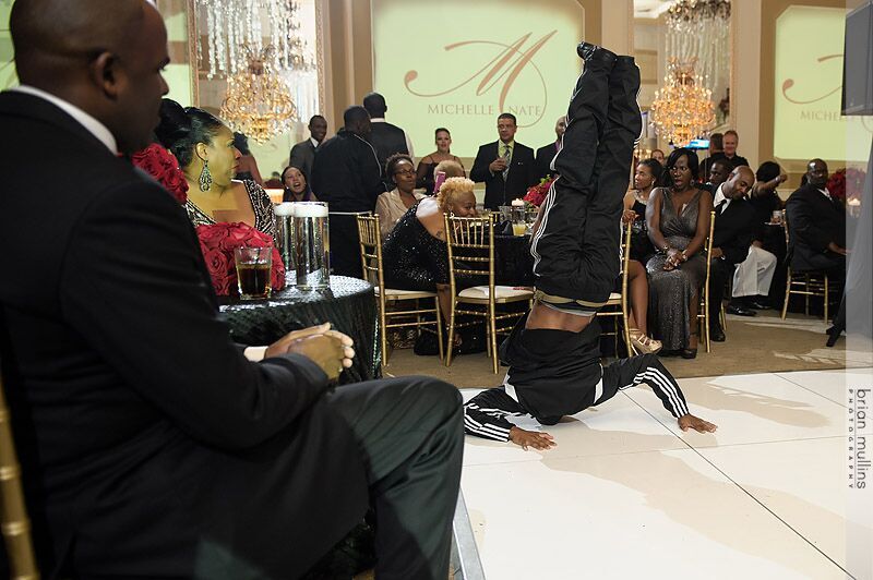 Breaker/B-boy balanced on the back of his head and neck during a choreographed performance at an event in a ballroom