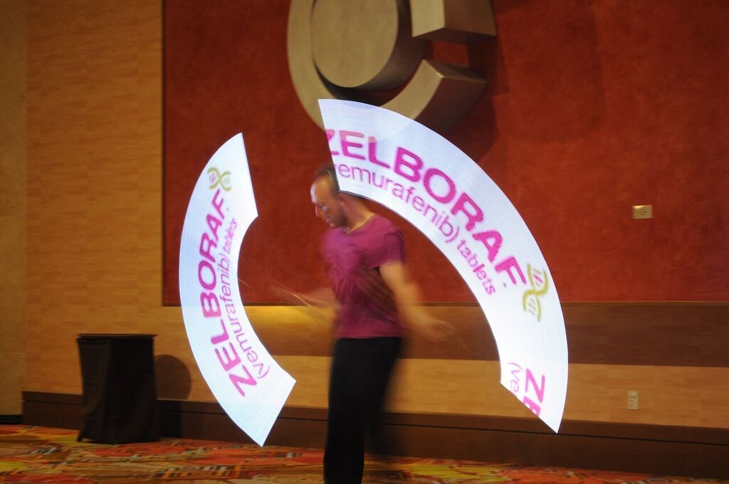 Performer spinning LED Poi creating a design of a corporate logo in the air