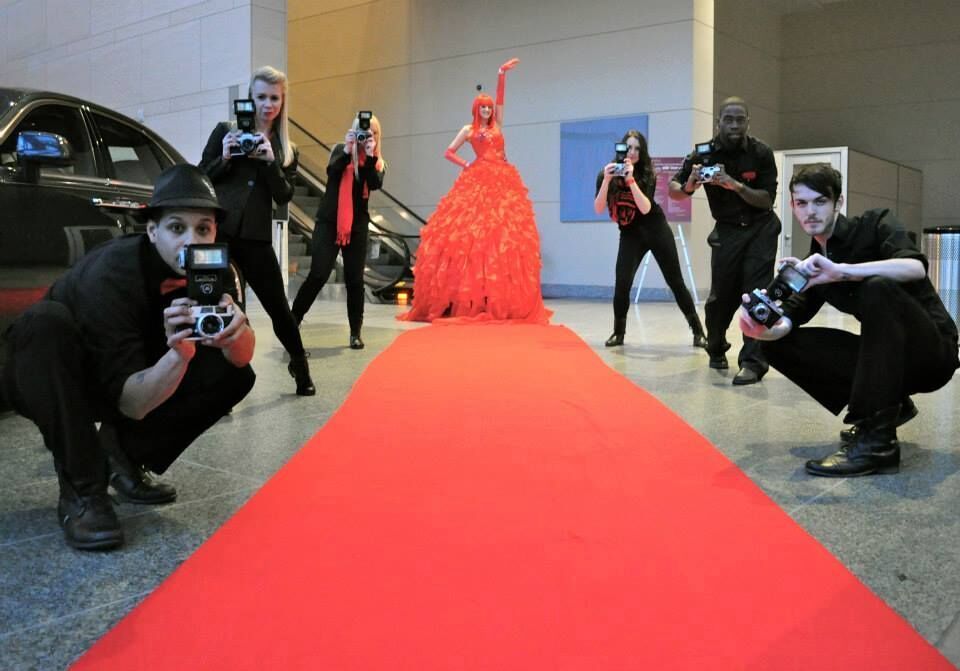 Red Carpet turns into a taller than average performer and her long red dress flanked on either side with six paparazzi performers