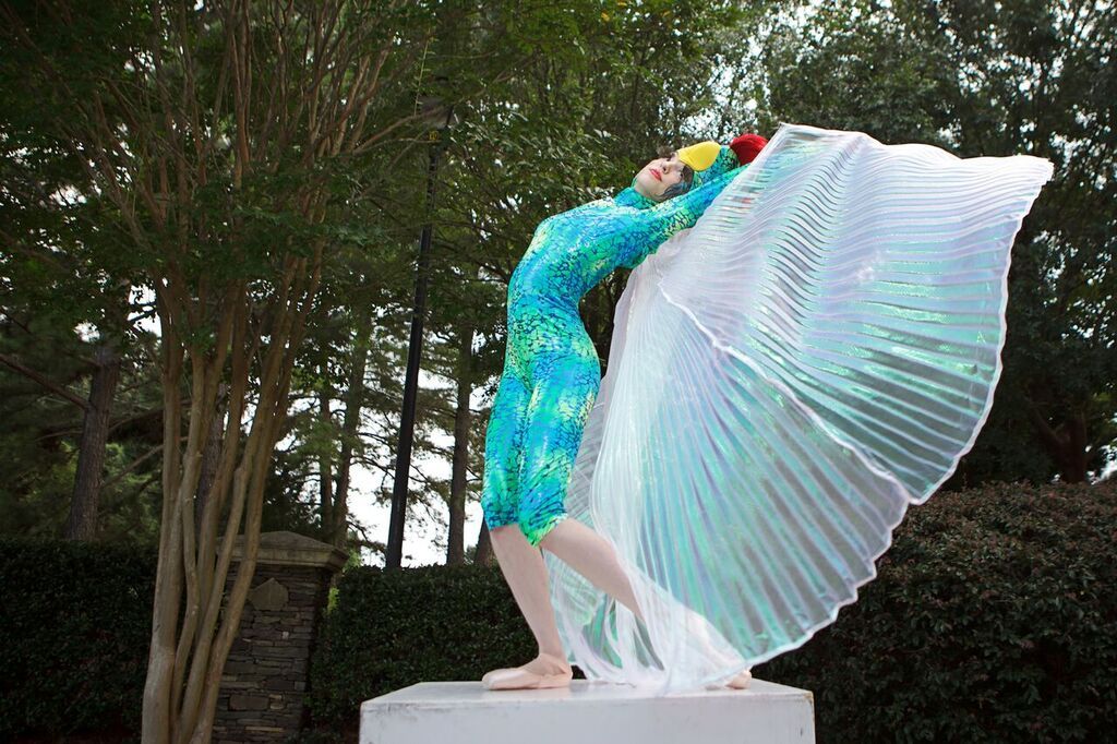 Bird Ballerina Performer dancing en pointe in a blue and green costume with iridescent wings and the face of a bird on her head