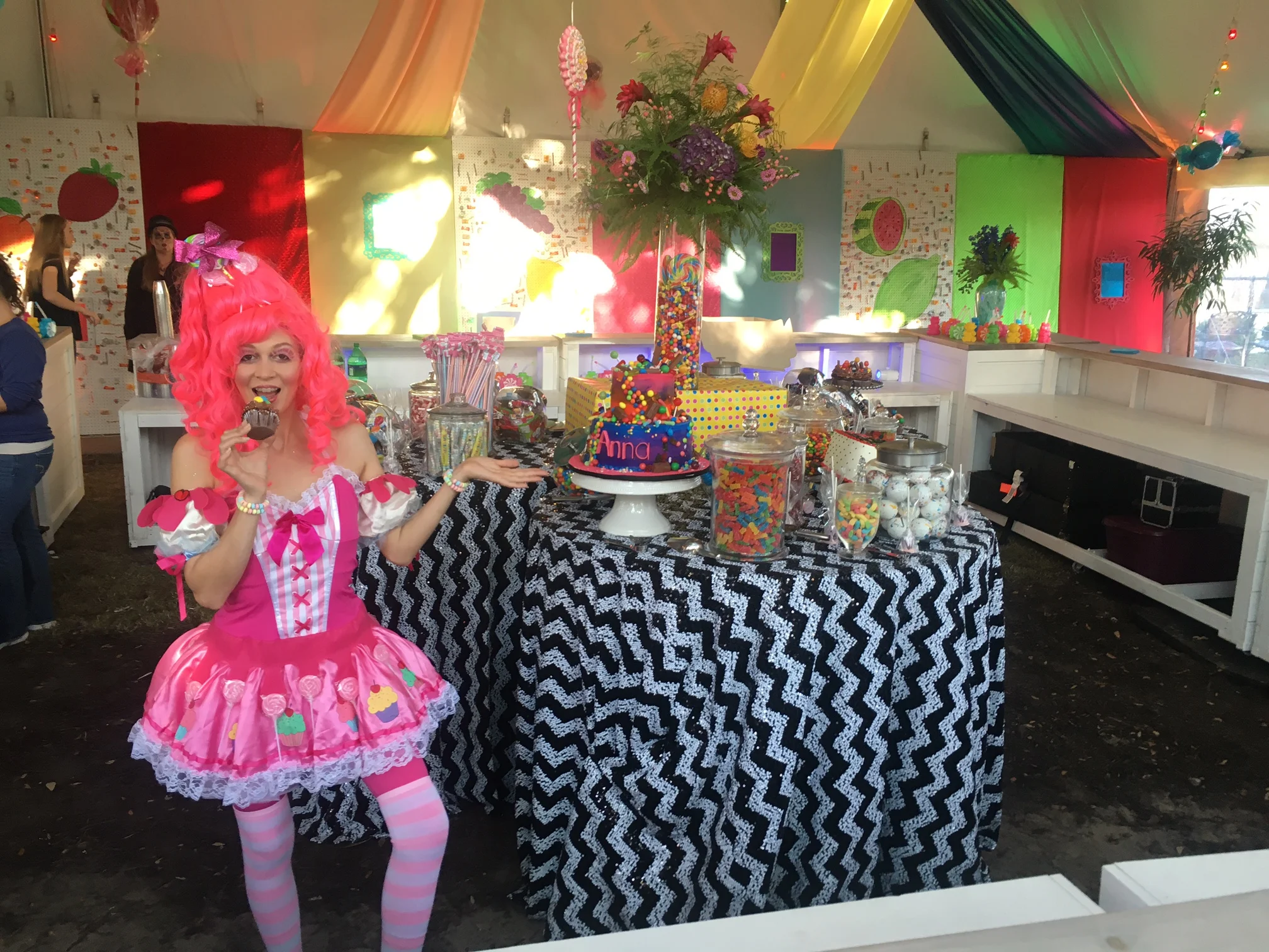 Strawberry Shortcake inspired costumed character posing for a photo in front of a table with a black and white zig zag tablecloth and lots of sweet treats