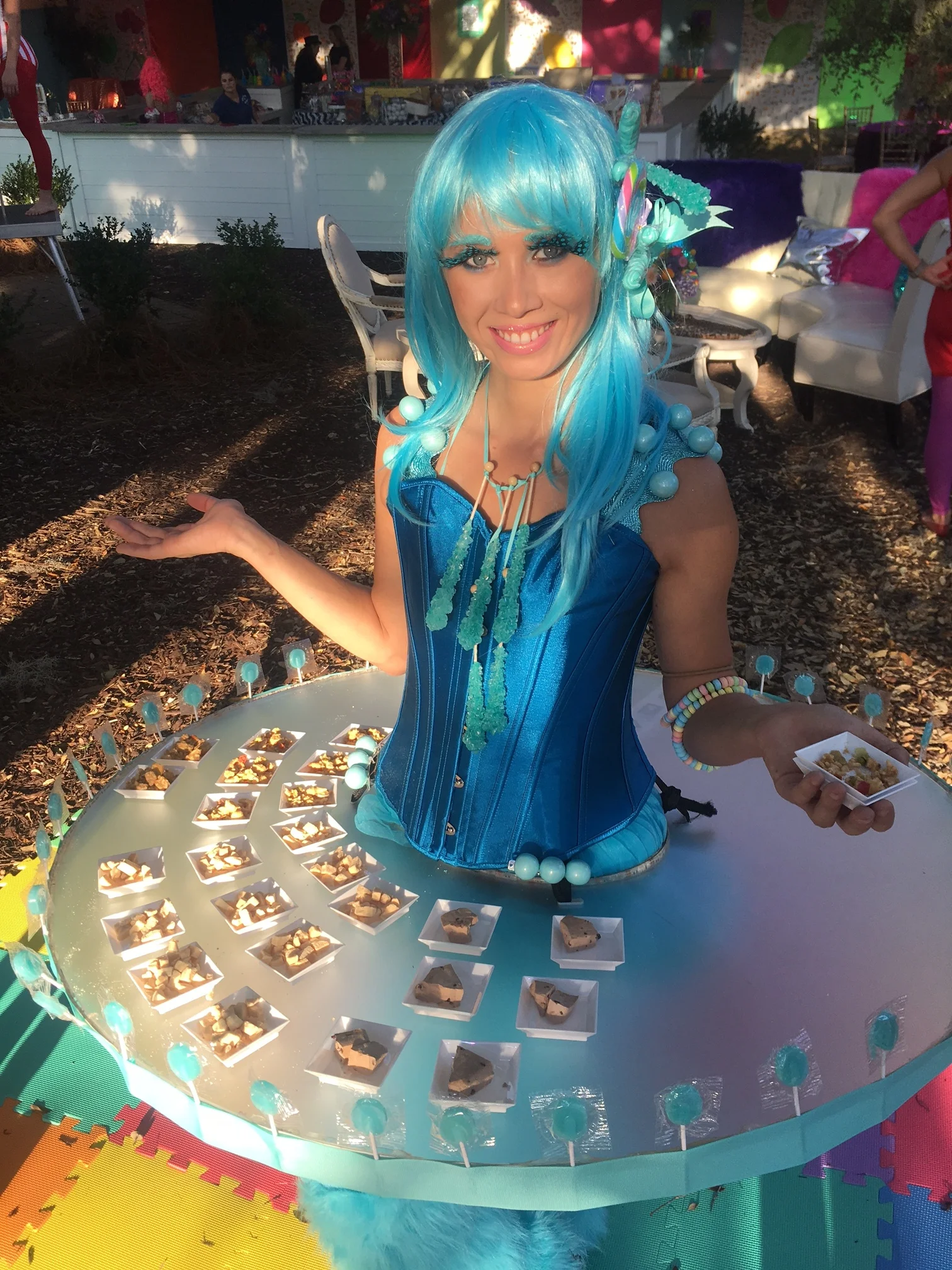 LED table performer costumed in a blue corset and blue wig, serving hors d'oeuvres at an event