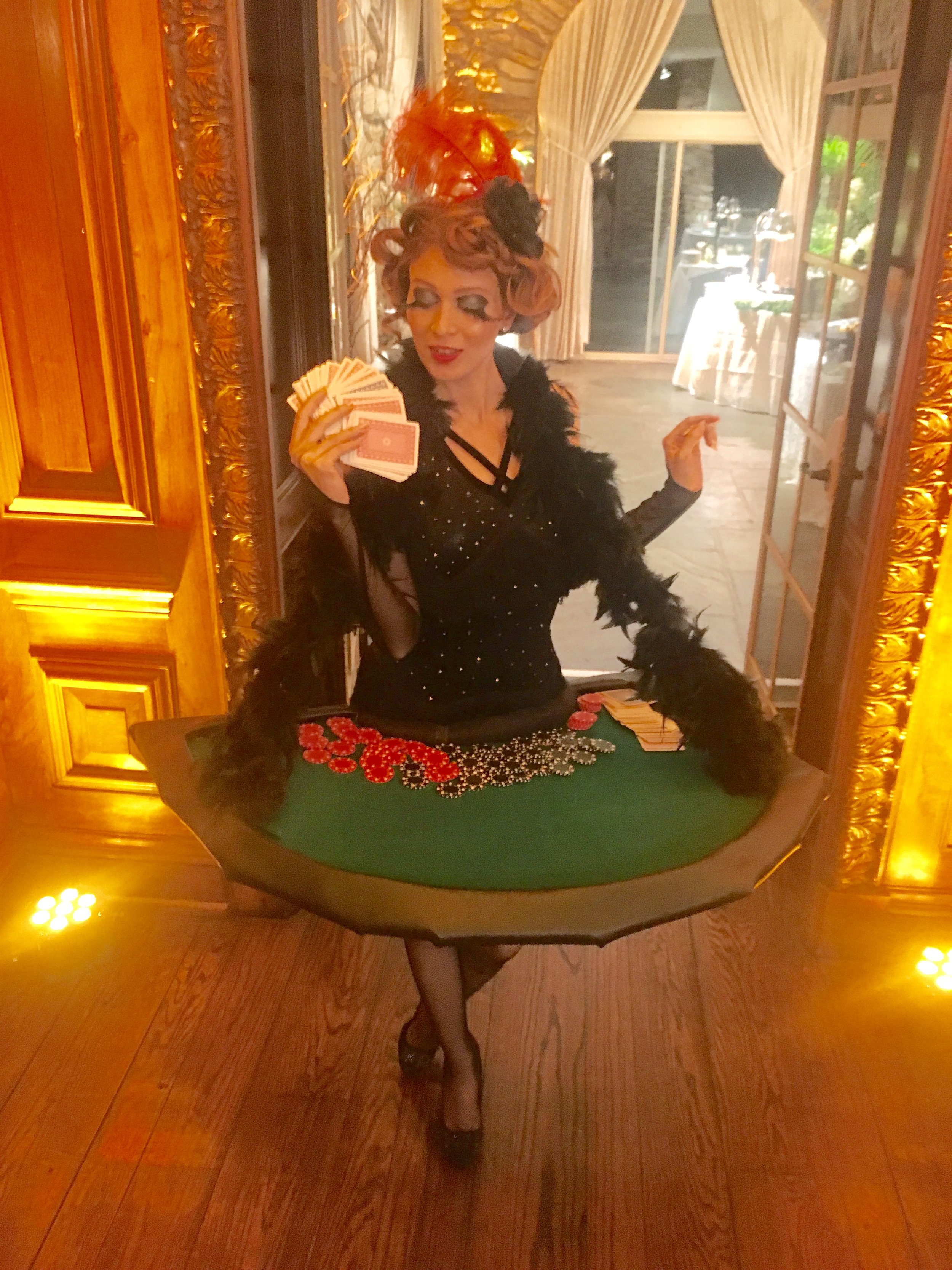 Flapper performer in a black fringe costume, gloves, feather boa, and feather headpiece carrying a mobile blackjack table for a 1920s themed event