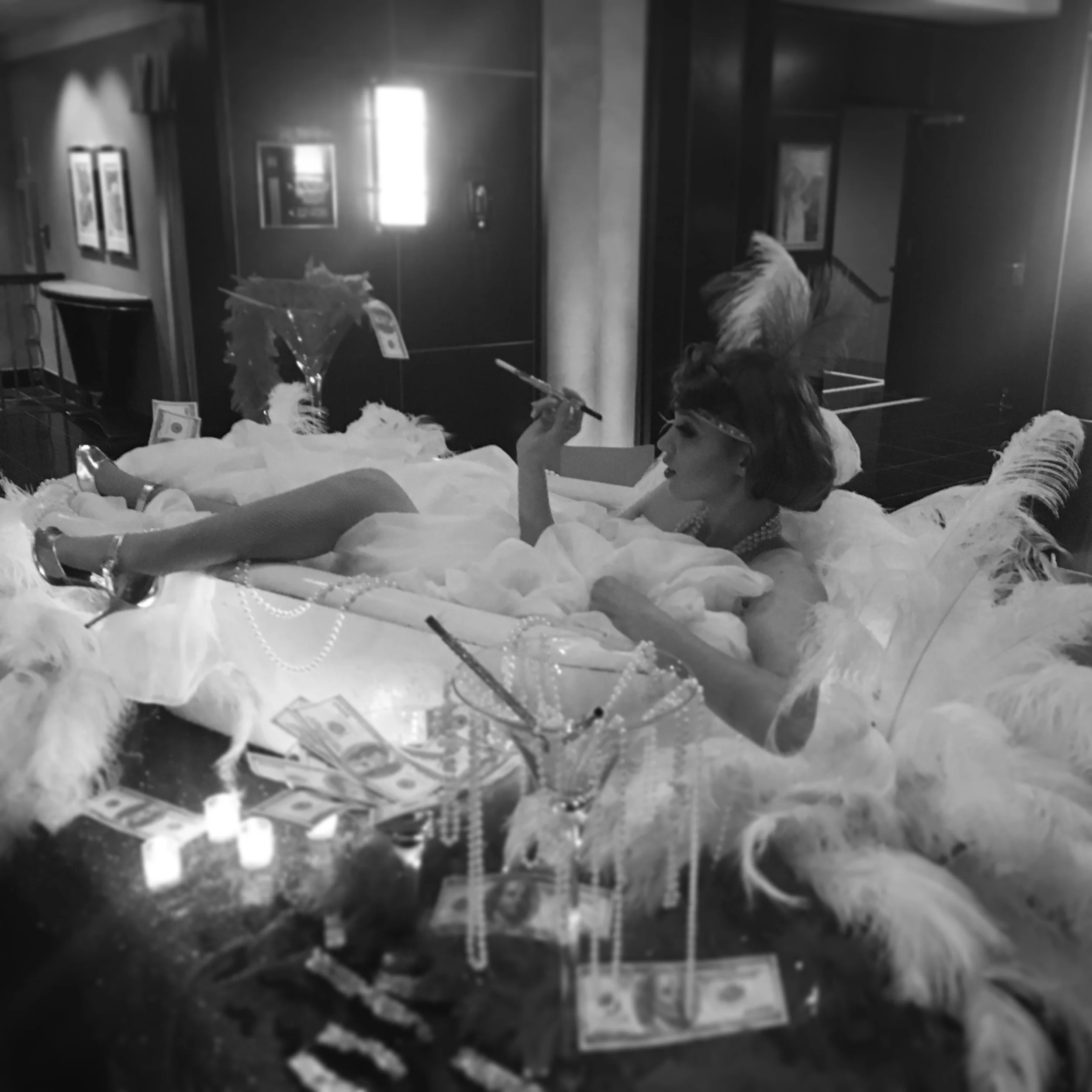 Performer lounging in a bathtub filled with white feathers at a 1920s themed event