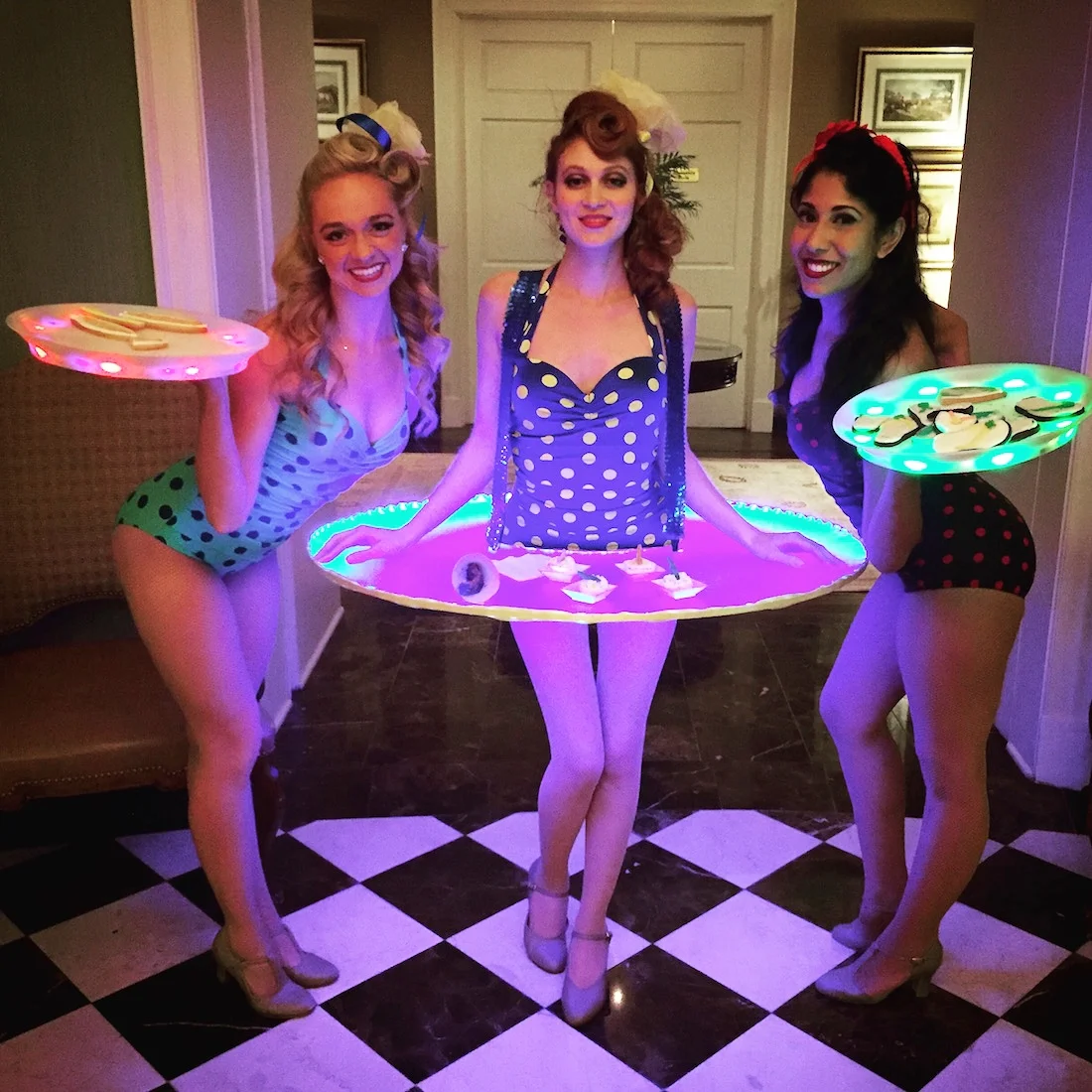 Three performers in retro style bathing suits serving hors d'oeuvres from either a tray or an LED skirt