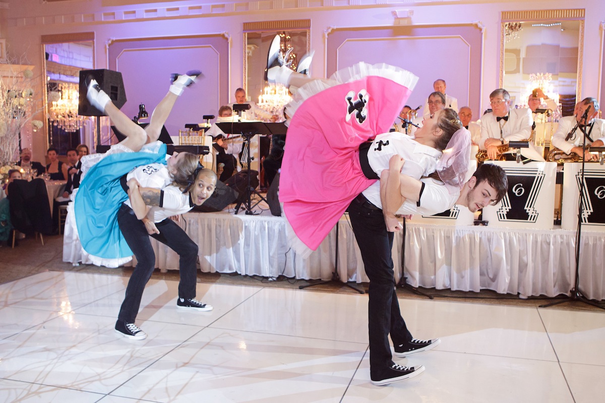 Four dancers performing a partner routine for a retro themed event. The two female dancers costumed in a blue or pink poodle skirt and the two male dancers in black slacks and a black and white polo.