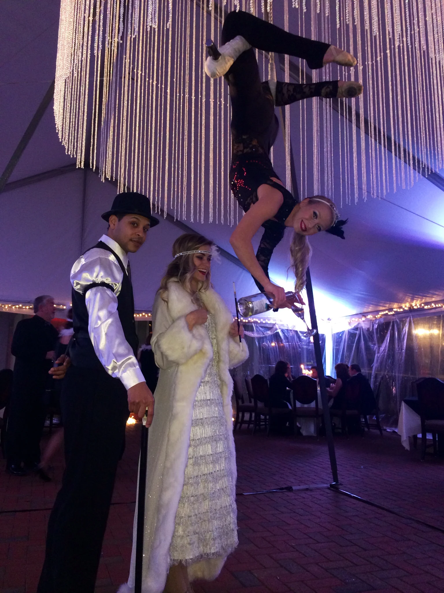 Aerial bartender on a trapeze inside an aerial chandelier pouring champagne upside down for guests at a 1920s themed event