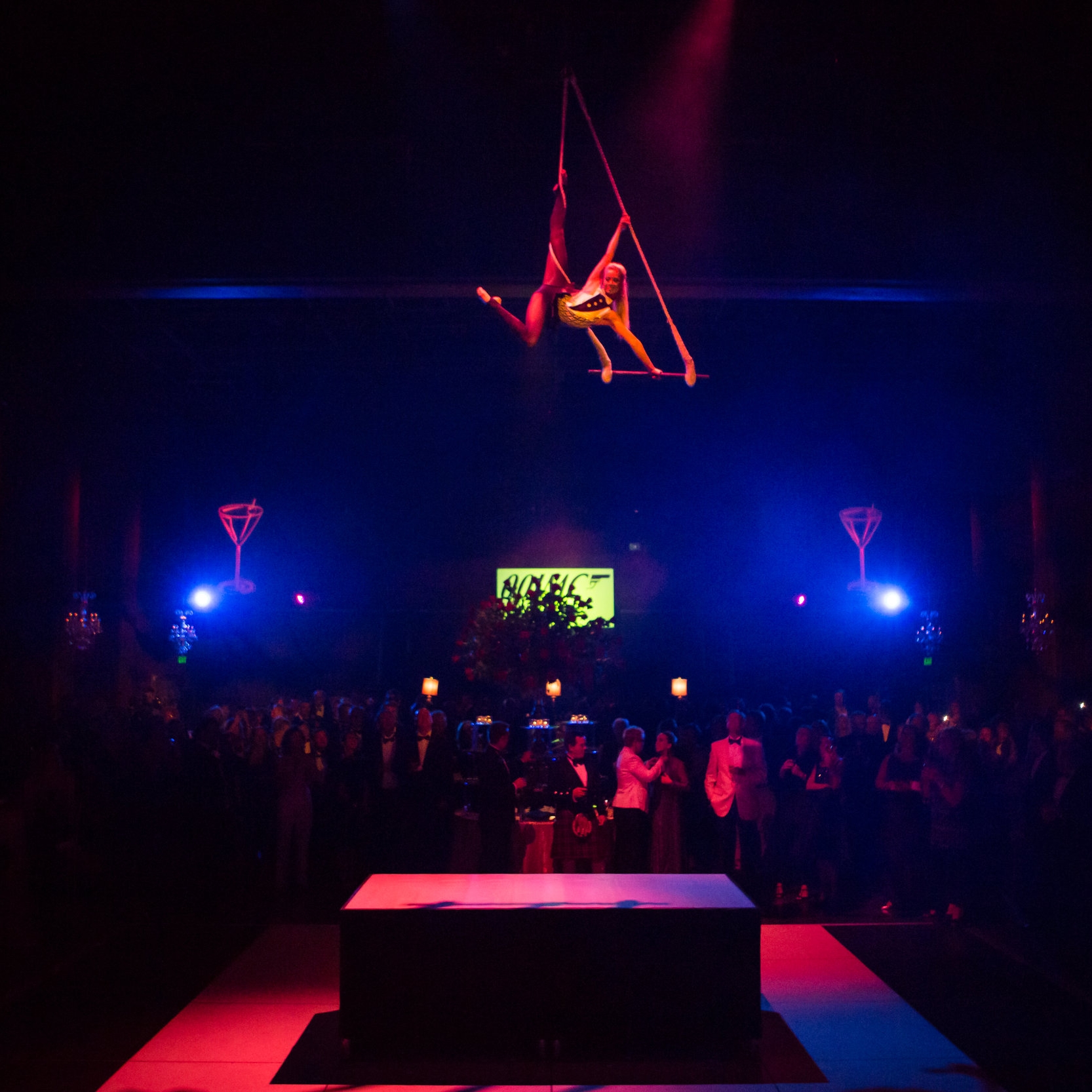 Aerialist performing on trapeze in a gold and black costume at a James Bond themed event