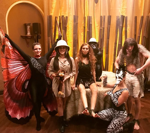 Performers for a jungle themed event; costumed as either cave people, a safari explorer, a zebra, or a red butterfly