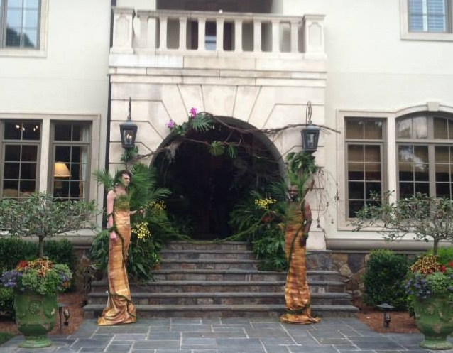 Two male grand entrance performers much taller than any guest in brown skirts and green leaves and branches adorning their torsos