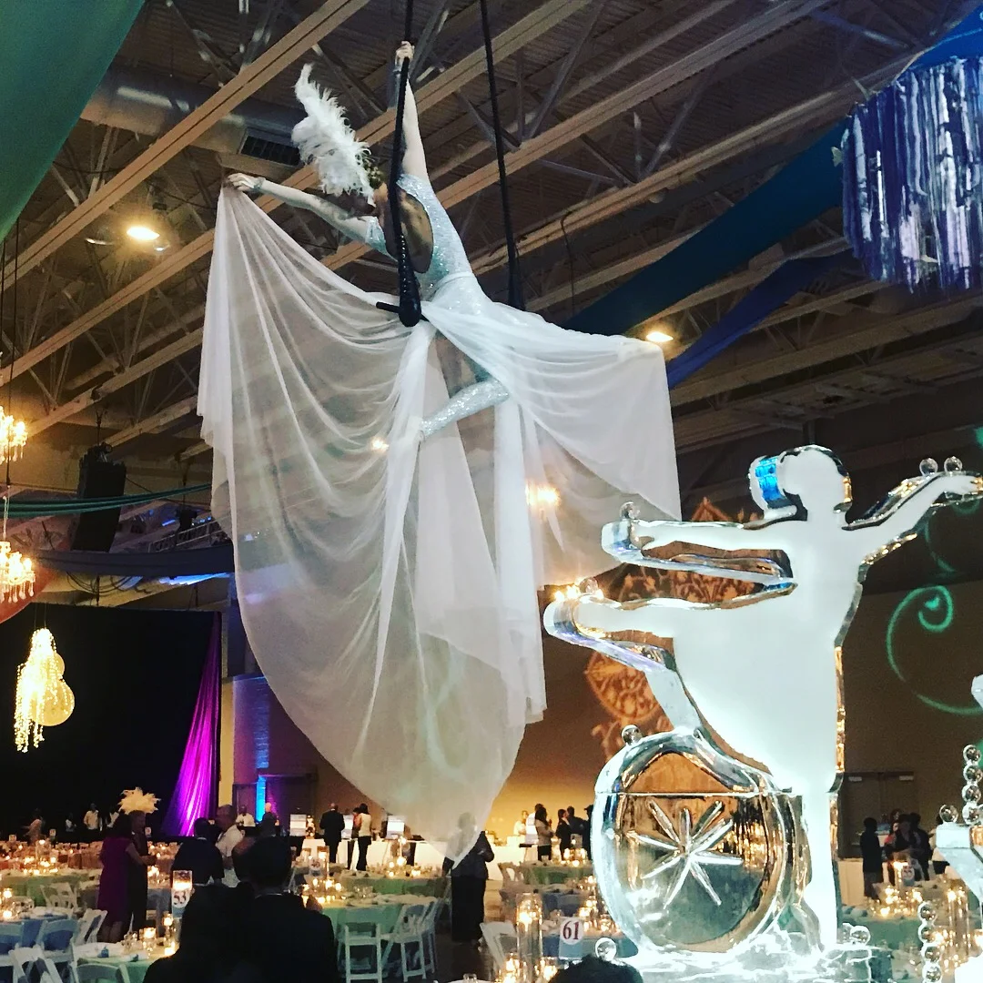 Aerialist performing on trapeze costumed in white with a huge tulle skirt at a winter holiday themed event