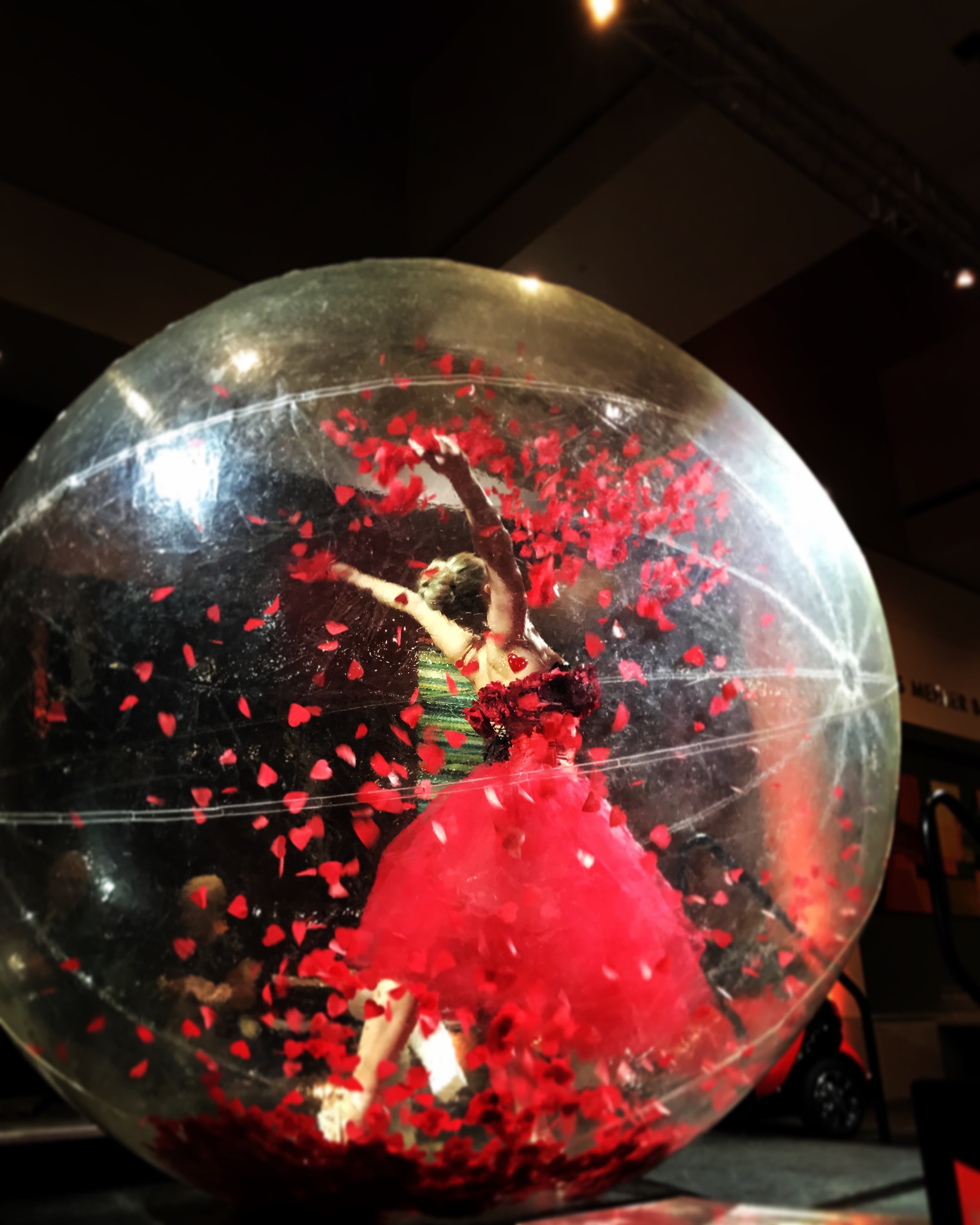 Life-sized snow globe with red heart confetti and ballerina performer inside costumed in a red tutu