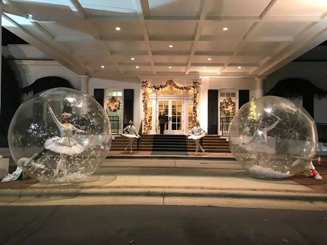 Four ballerinas costumed in white tutus on either side of the grand entrance to an event, two ballerinas inside larger than life snow globes with white paper snow inside