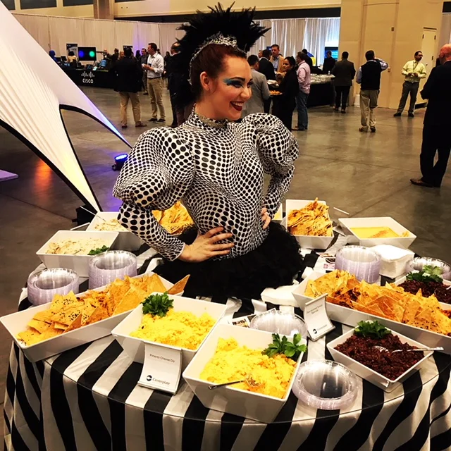 Performer costumed in an eclectic black and white pattern living inside a large round table serving food for guests at an event