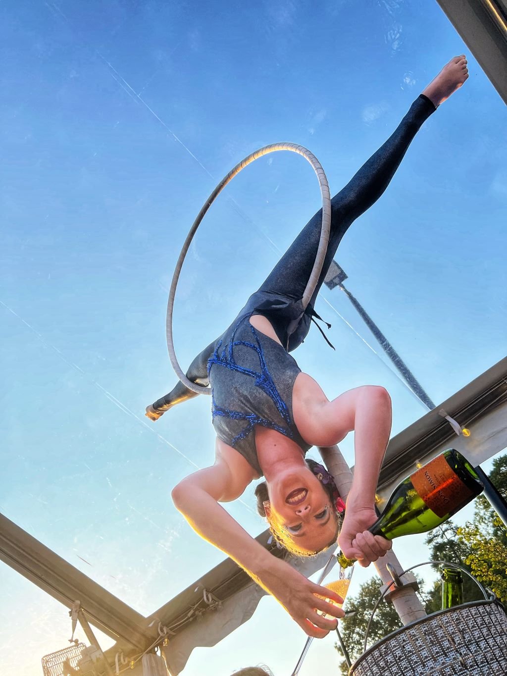 Aerial bartender pouring a glass of champagne upside down on a Lollipop Lyra in a grey and blue costume