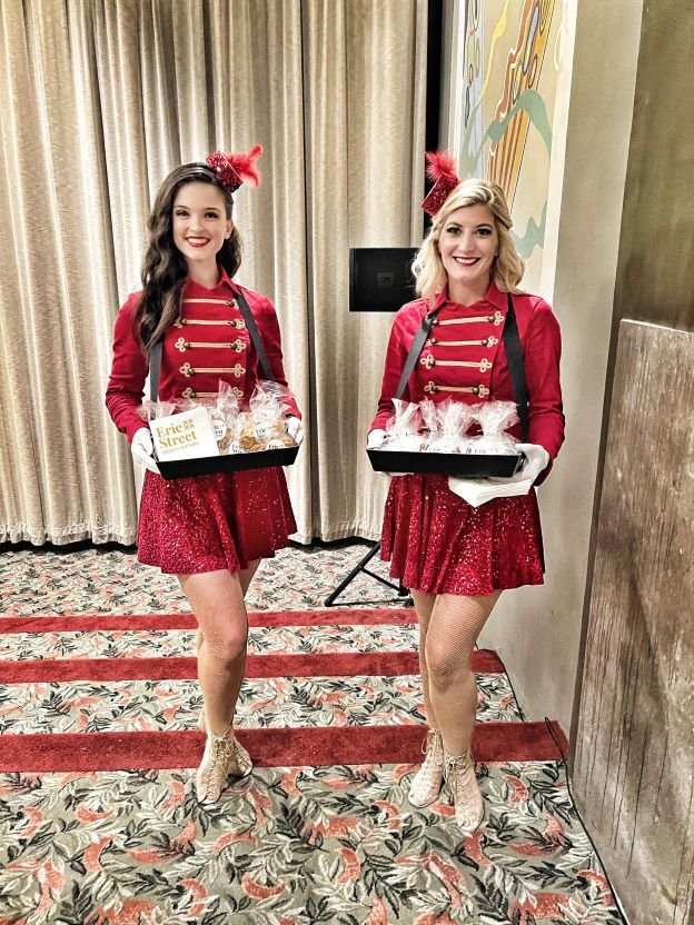 Two bell hop themed performers in red costumes holding cigarette trays to pass party favors to guests at an event in Charleston, South Carolina