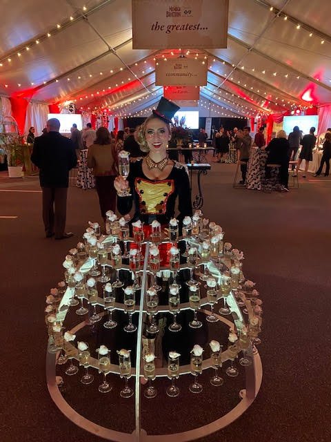 Champagne dress performer in a ring master inspired costume and top hat surrounded in a metal skirt covered in champagne flutes ready to head to guests at a circus themed event
