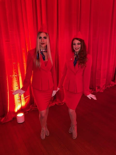 Two retro style flight attendant performers in red costumes at an event