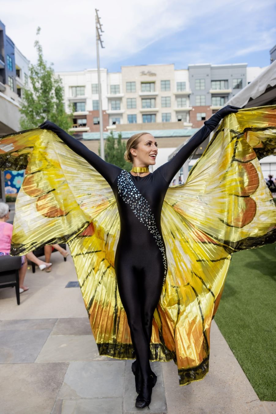 Butterfly Ballerina performer in black costume and huge yellow butterfly wings dancing outside an at outdoor event