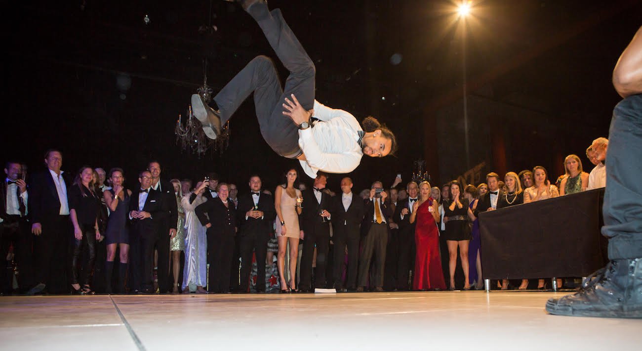 Breaker/B-boy performing a backflip on a dancefloor during a choreographed performance at a James Bond themed event