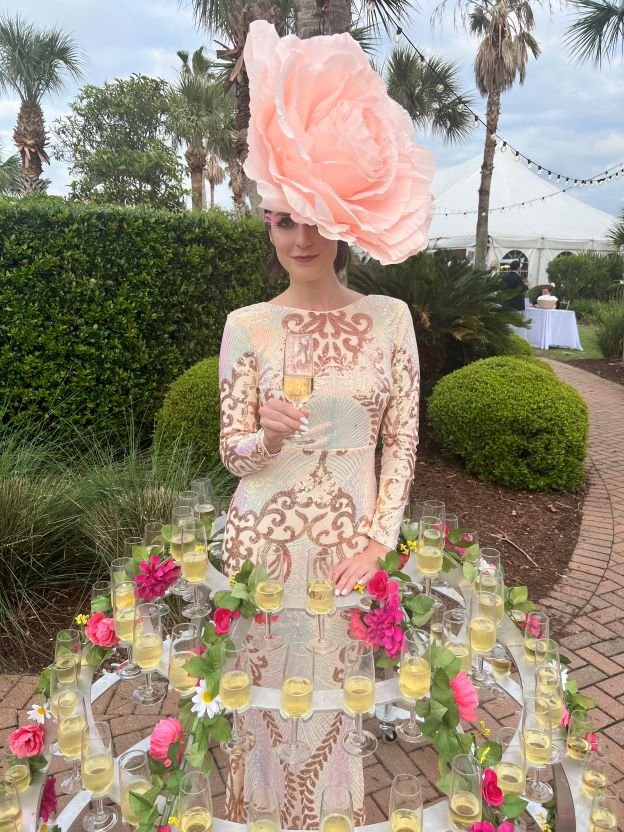 Performer in a metal champagne skirt, her skirt made of champagne flutes and pink flowers, costumed in a pink and rose gold gown with large pink flower in her hair at an outdoor event in Charleston SC