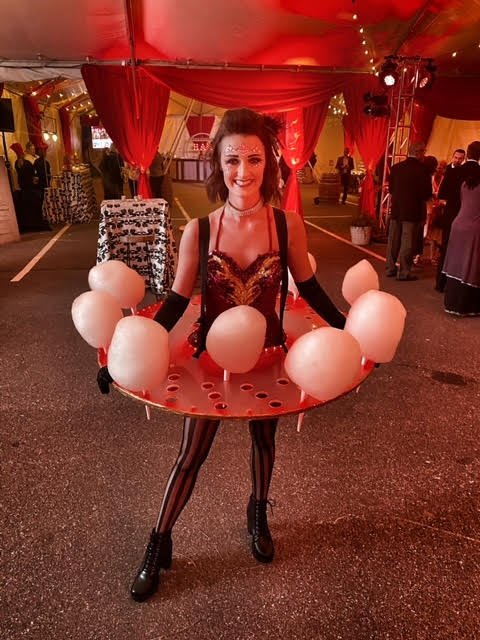 Performer with a table around her waist and inserts for cotton candy in the table dressed in a red and black costume for a circus themed event