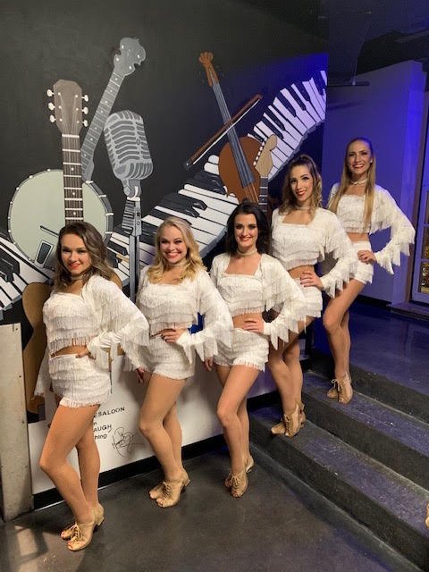 Five country line dancers in white fringe costumes and heels