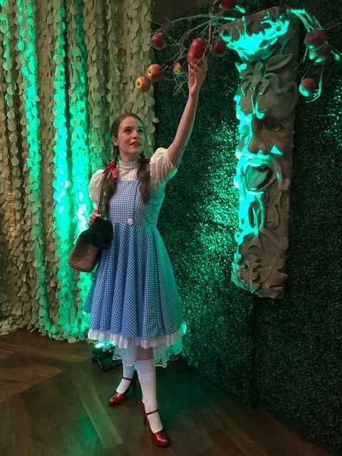 Dorothy inspired character reaching for an apple on a tree at a Wizard of Oz themed event