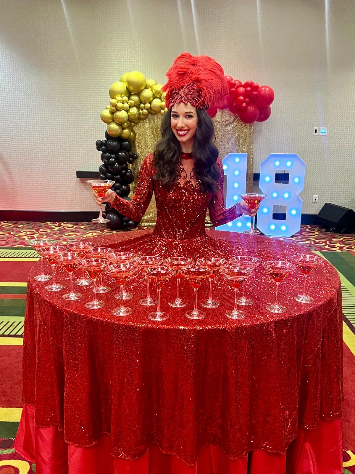 Performer costumed in red living inside a large round table serving specialty cocktails for guests at an event