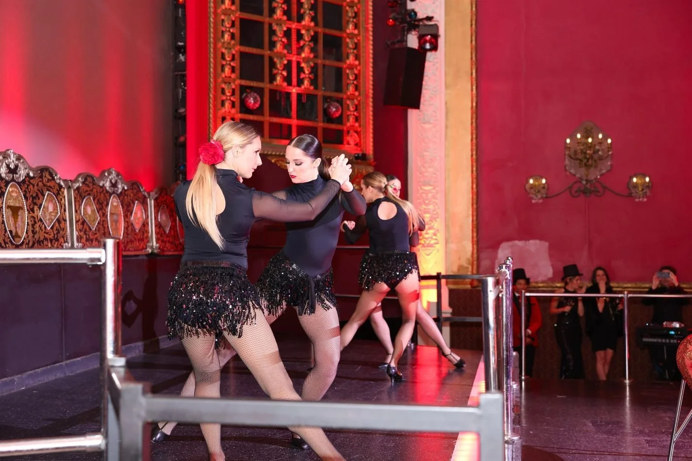 Four female dancers performing a choreographed tango inspired routine costumed in black with red rose hairpieces during a Moulin Rouge themed dinner theater event