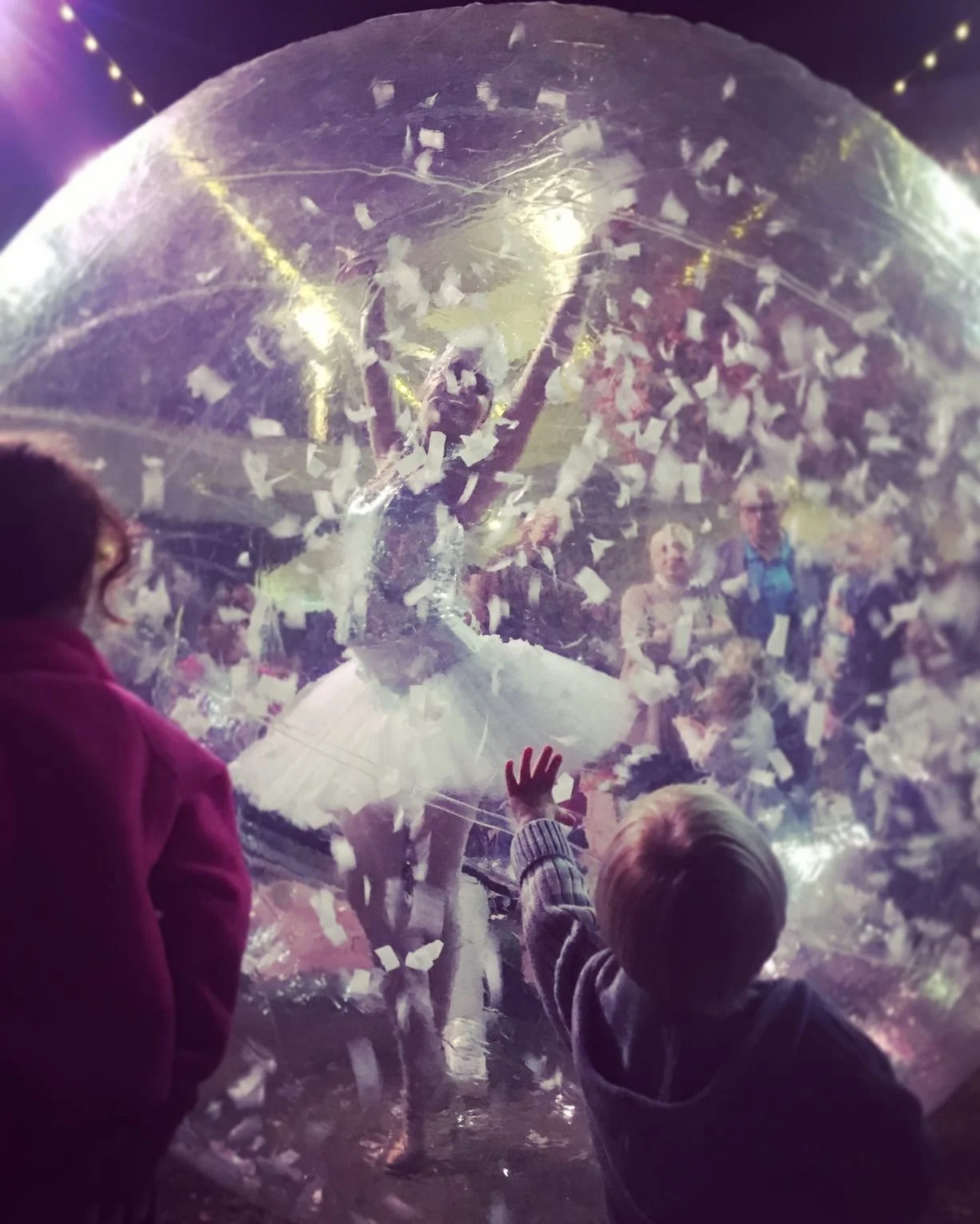 Life-sized snow globe with white snow confetti and ballerina performer inside costumed in a white tutu