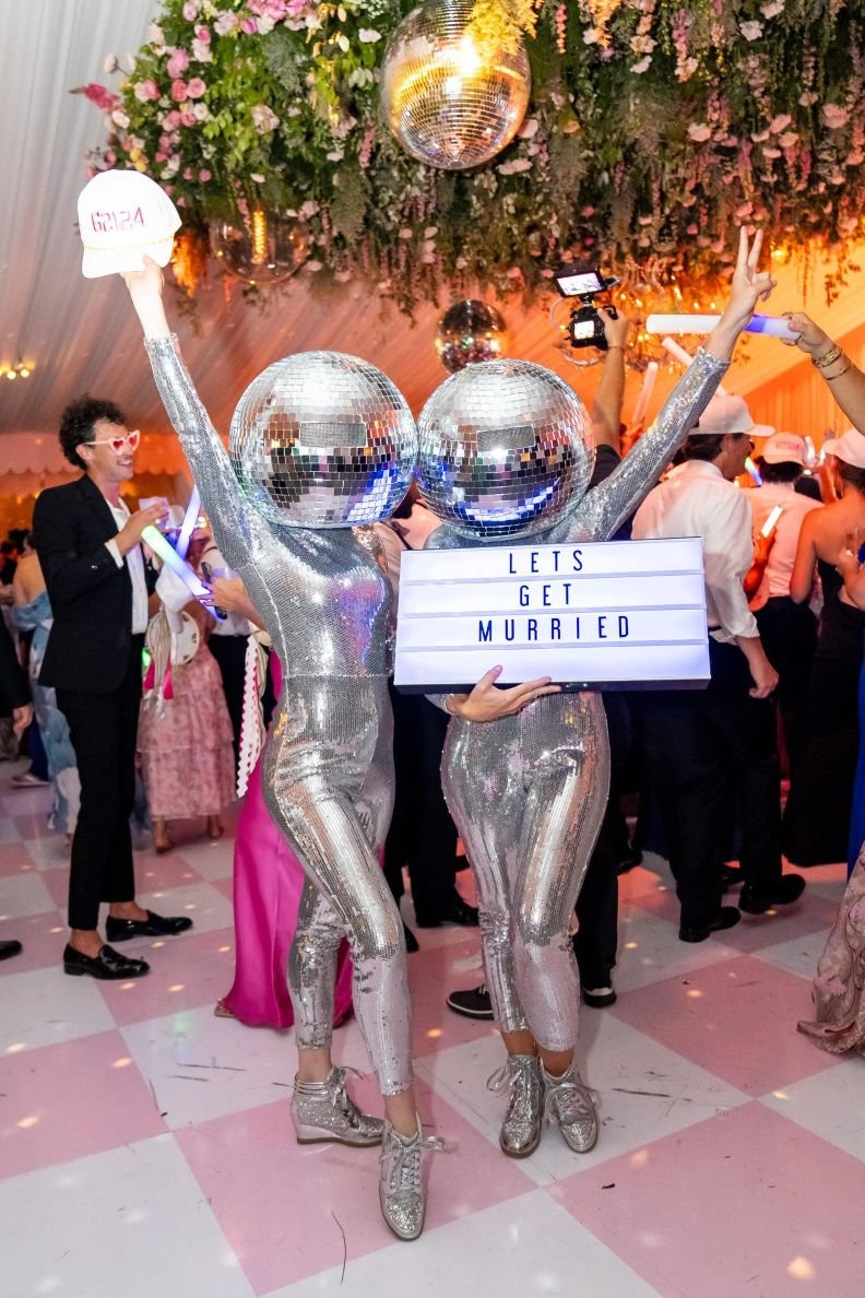 Duo Disco Ball Dancers Holding Party Favor Hats and Custom Sign at Wedding