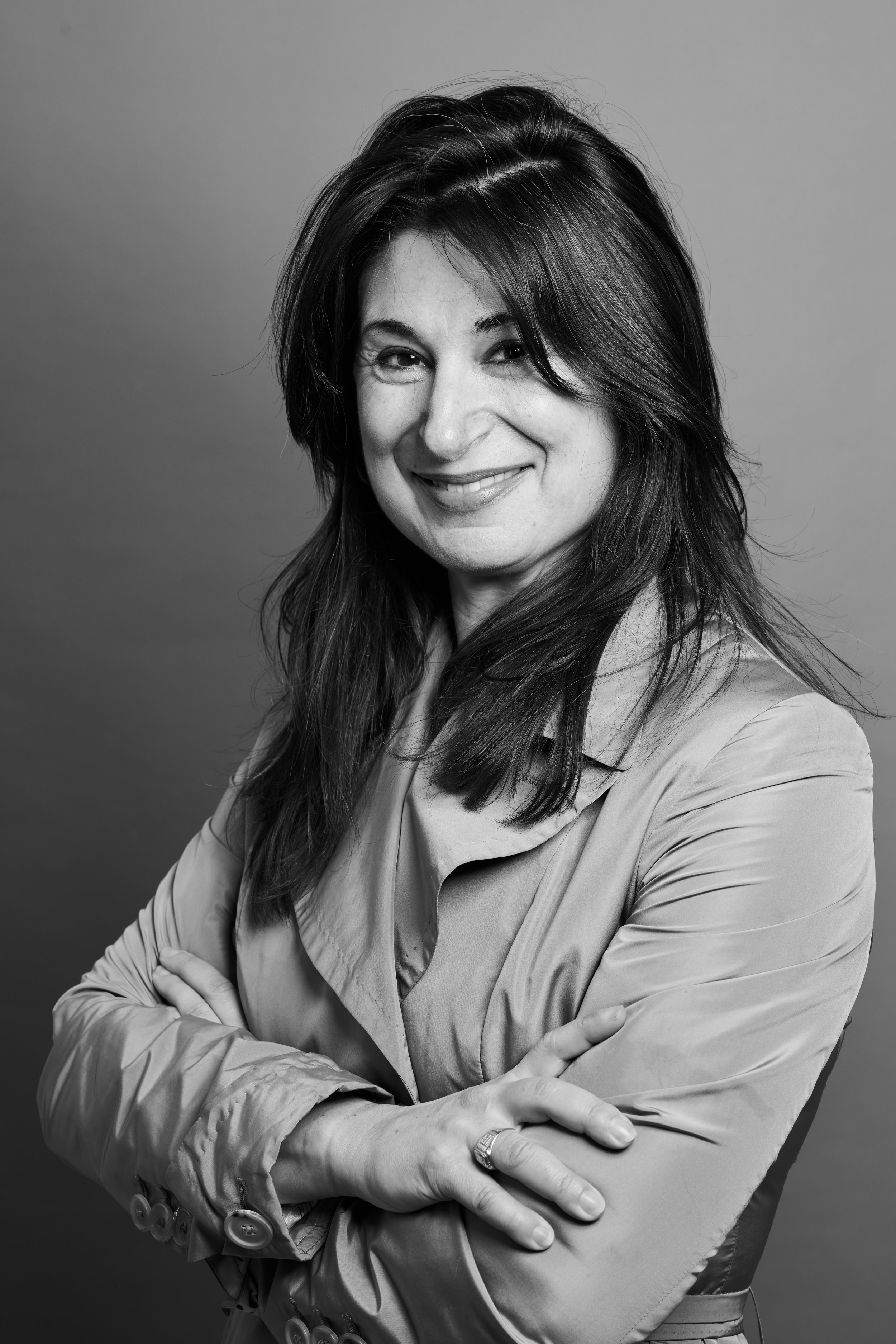 Black and white portrait of a woman smiling with arms crossed, wearing a buttoned shirt.