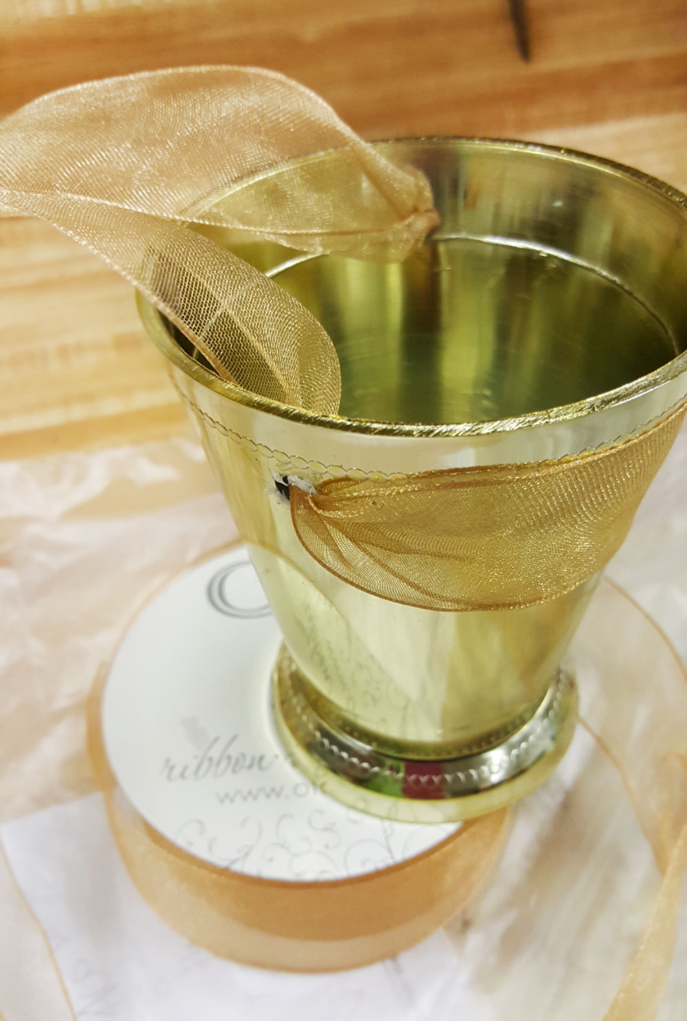 Next, thread your favorite wired ribbon through the holes. We like ours to be on the outside of the front of the cup, to give it the most stability preventing anything from spilling forward. Wired ribbon works best, as it will not slip or slide as you tie the ribbon securely to the chair.