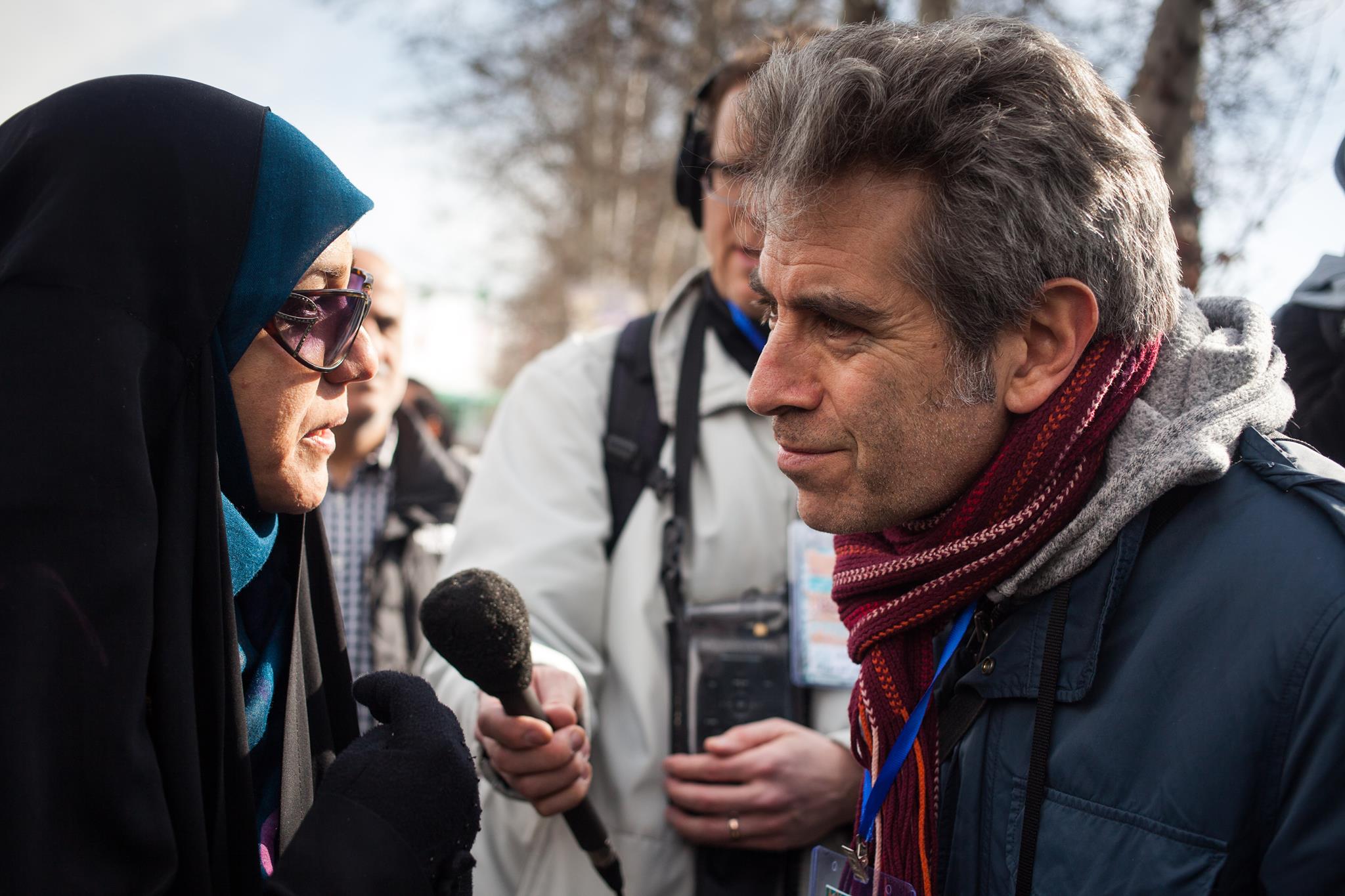 Host Marco Werman speaks with a school teacher at a rally in Tehran. (Credit: Mahya Rastegar)