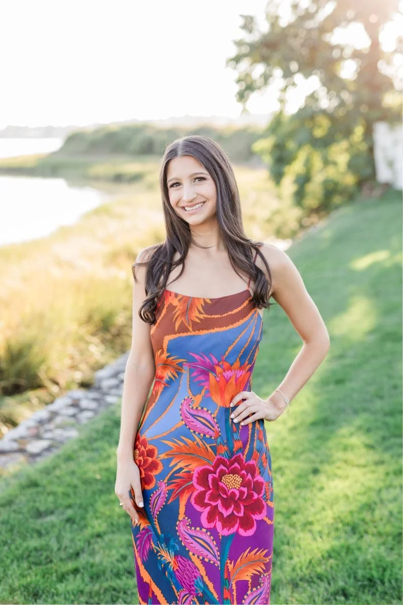 Young woman with long dark hair smiling outdoors on a sunny day.