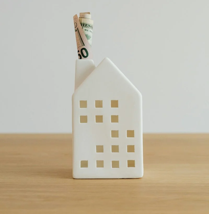 A white ceramic house-shaped pencil holder with a $50 bill tucked inside the chimney.