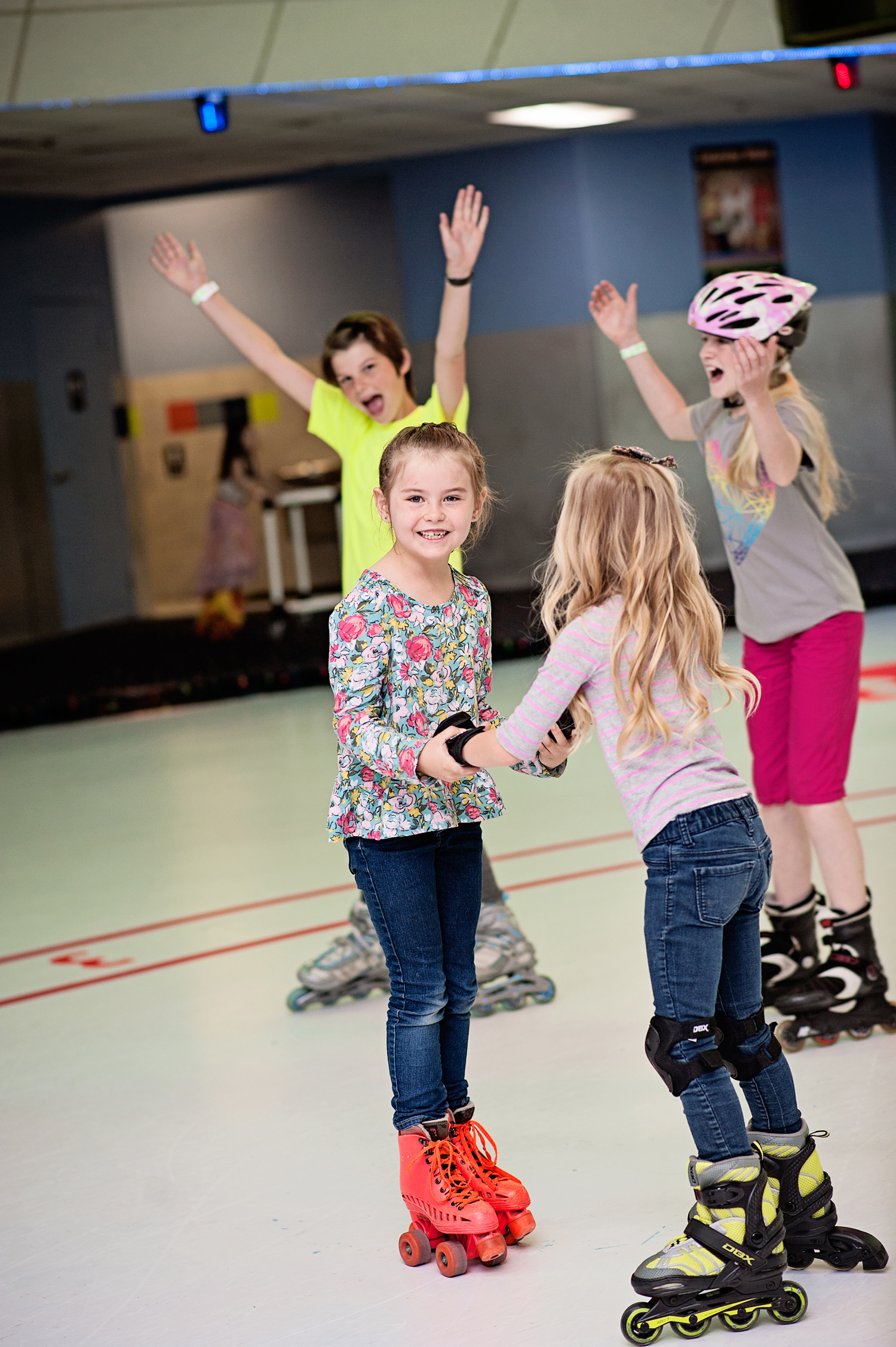  two young girls holding hands while rollerblading, while more kids enjoy skating 