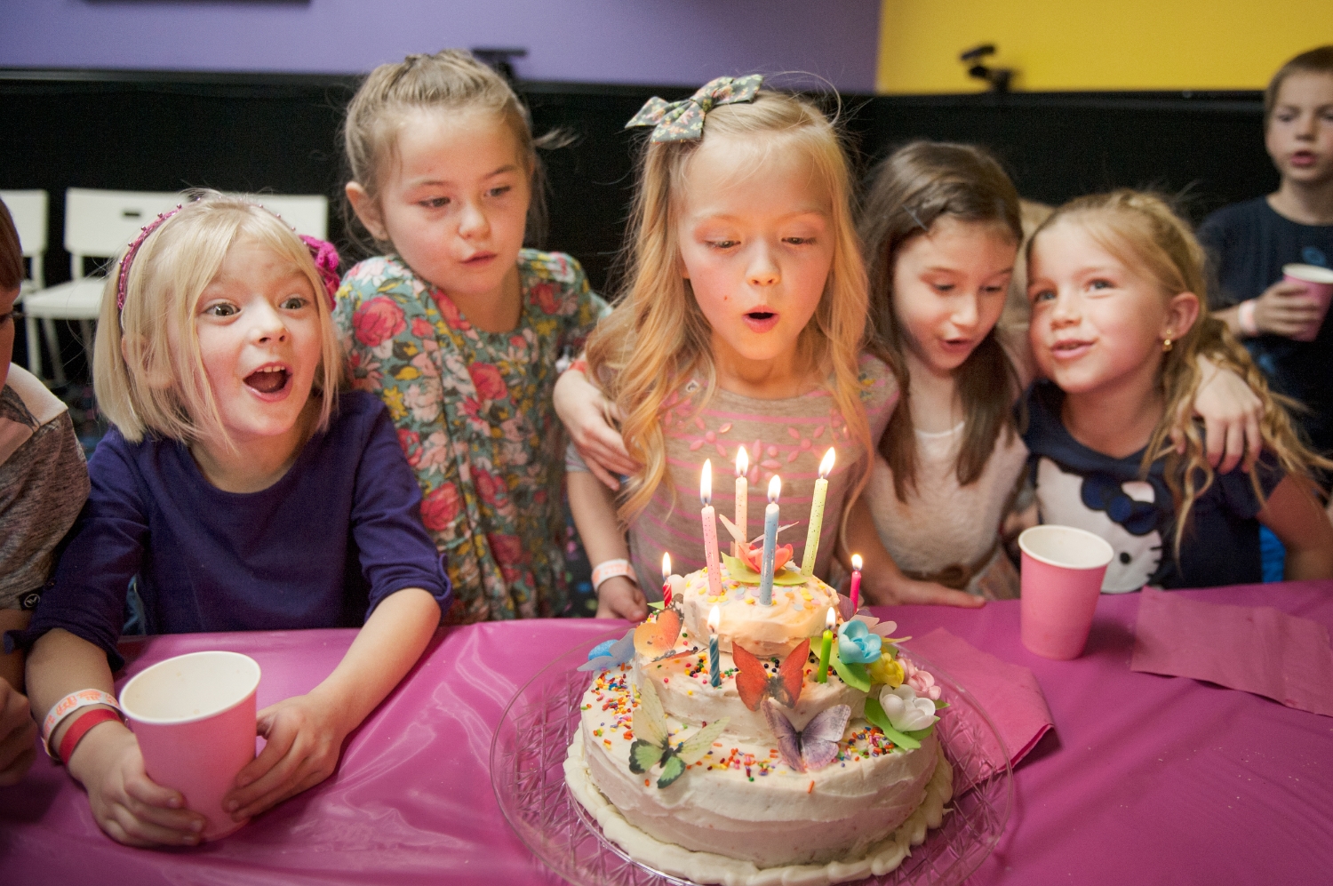  party gathers around as the birthday girl blows out the candles on her birthday cake 