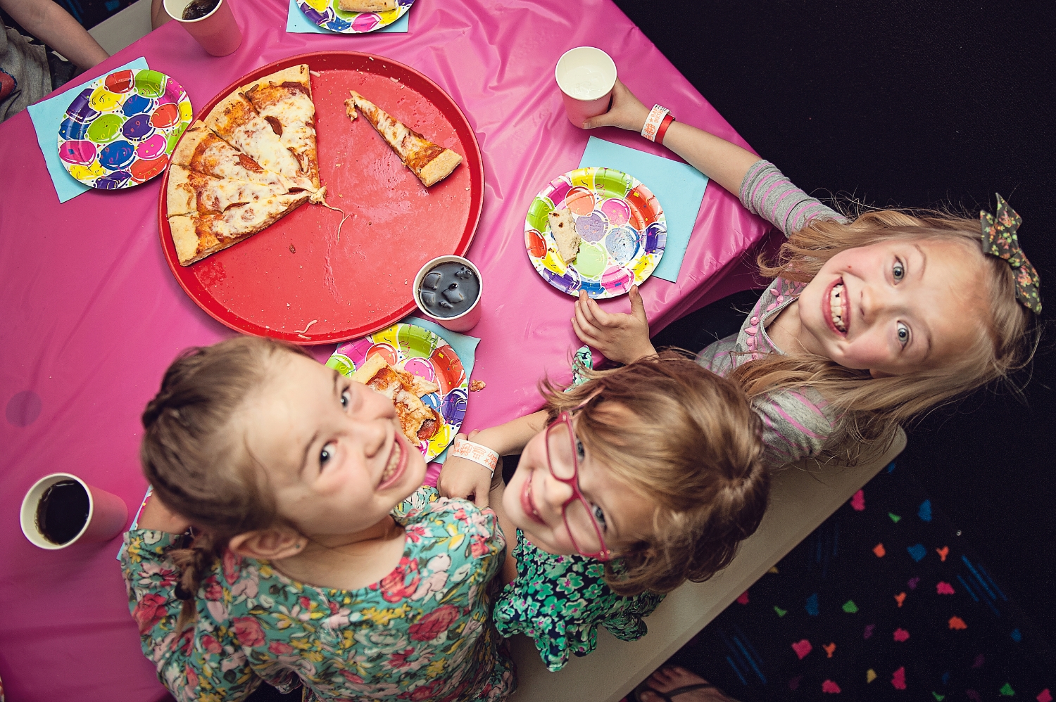  young girls looking up at the camera while eating pizza at a birthday party 