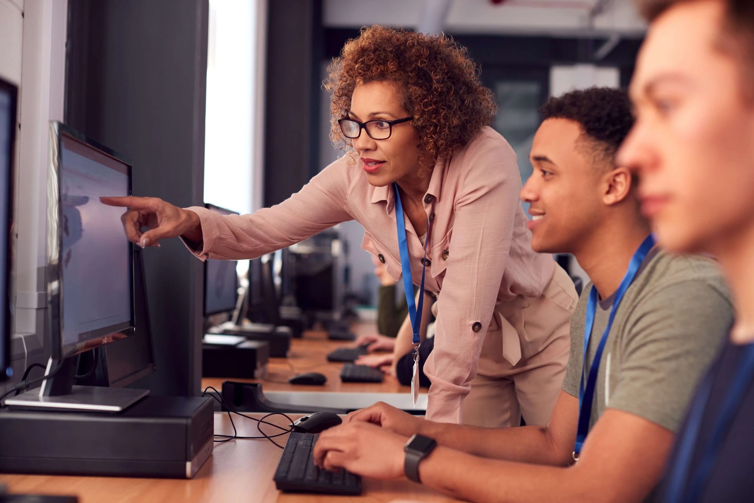 Two students sitting at computers while instructor points to a computer screen