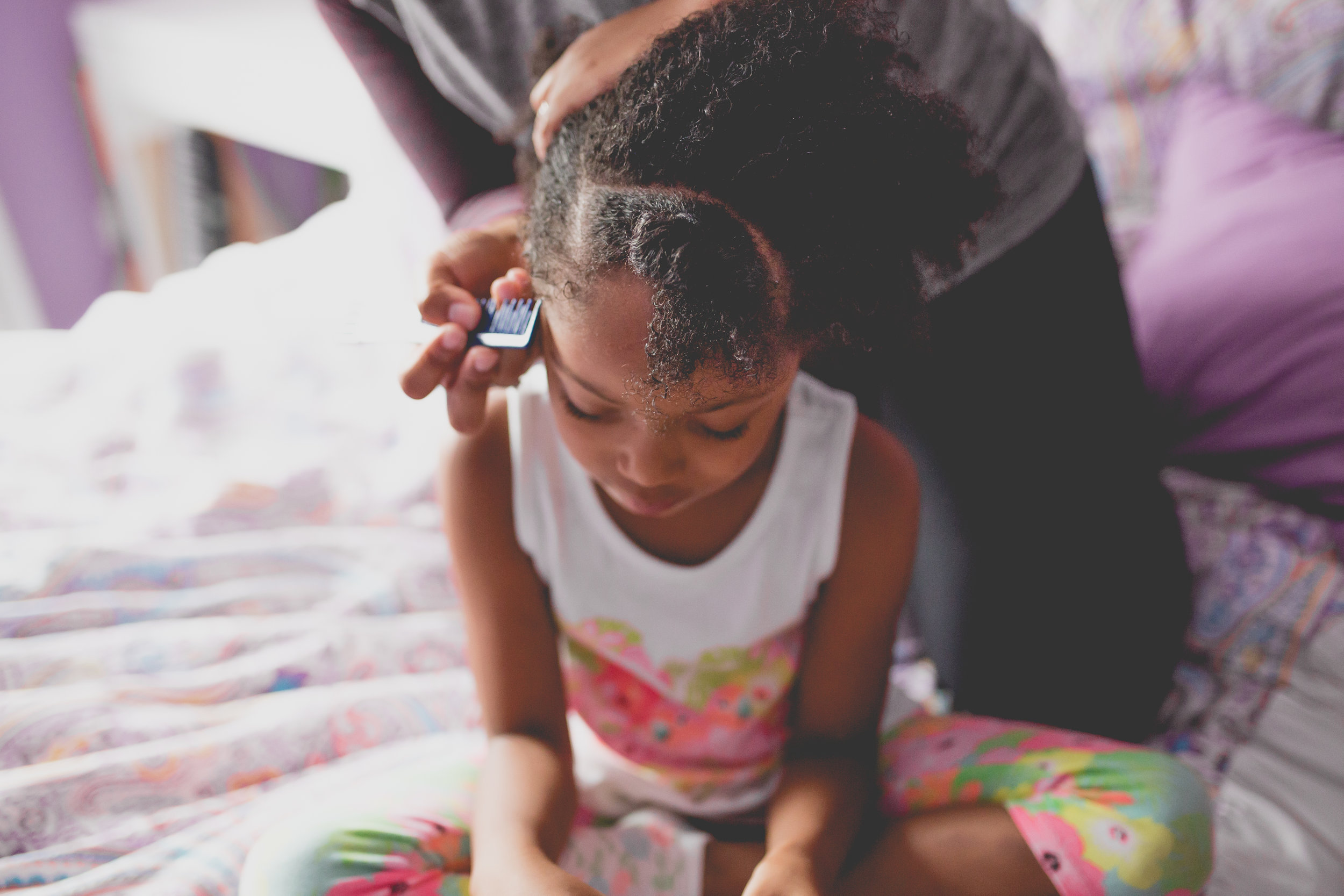 Girl looks down as mom parts her hair for cornrows