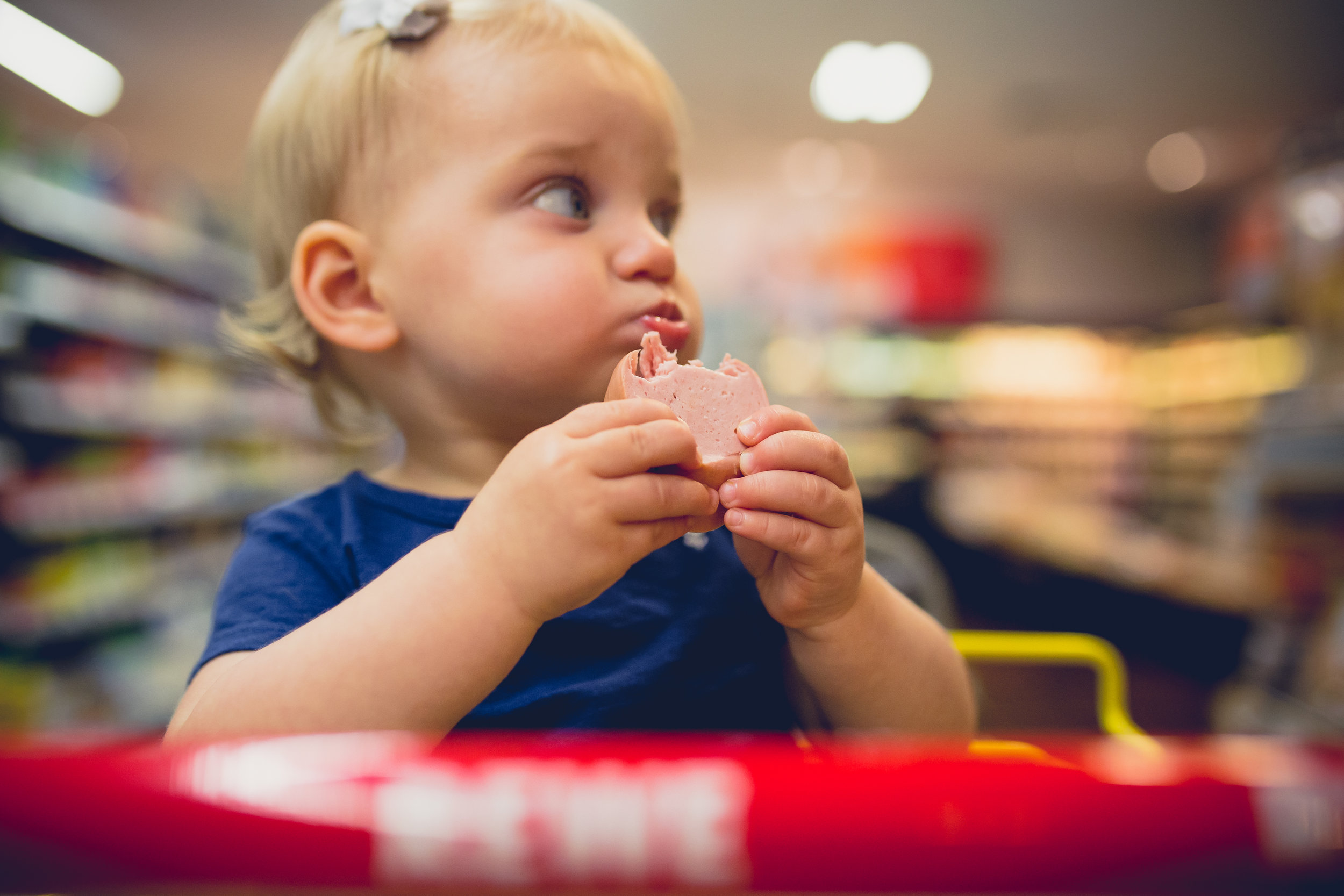 Toddler girl eats fleischwurst (bologna) in grocery cart