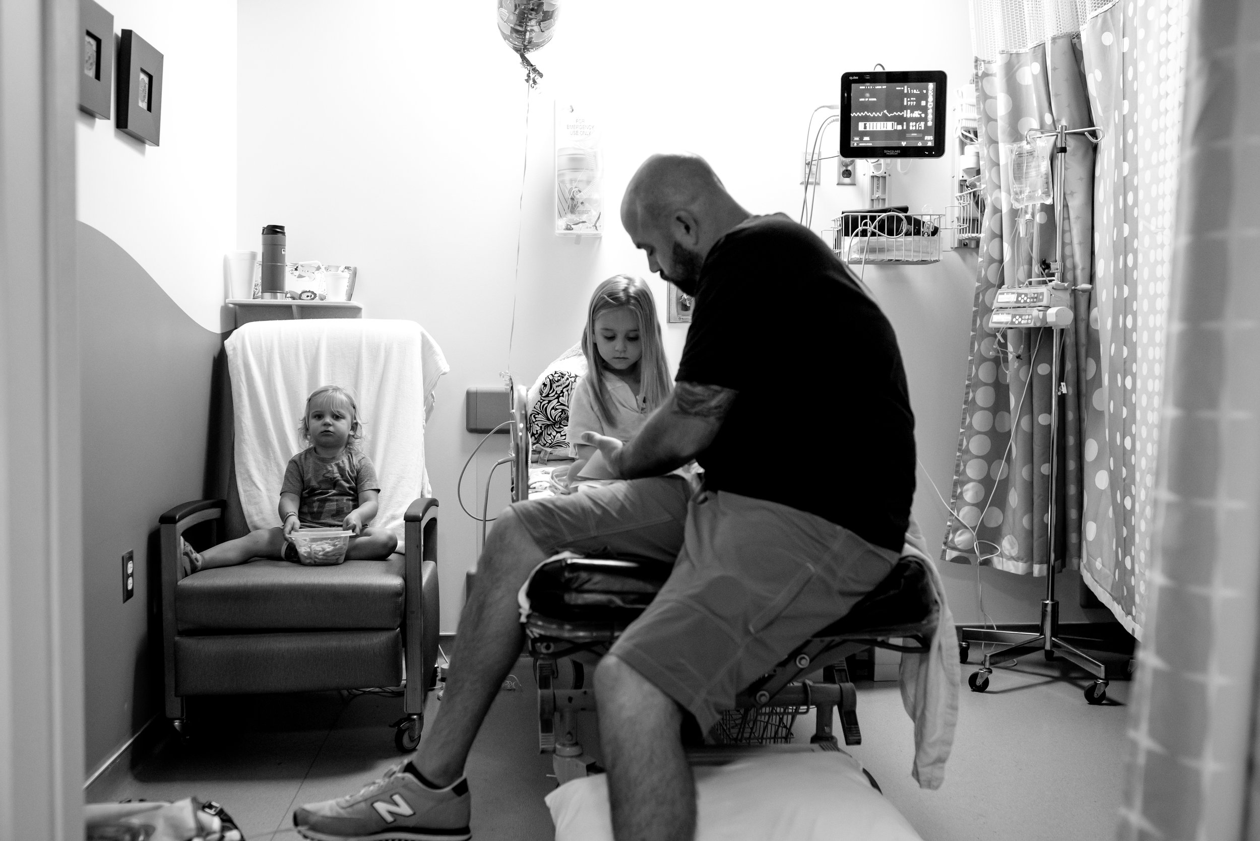 Dad and daughter look at book in hospital and girl eats snack