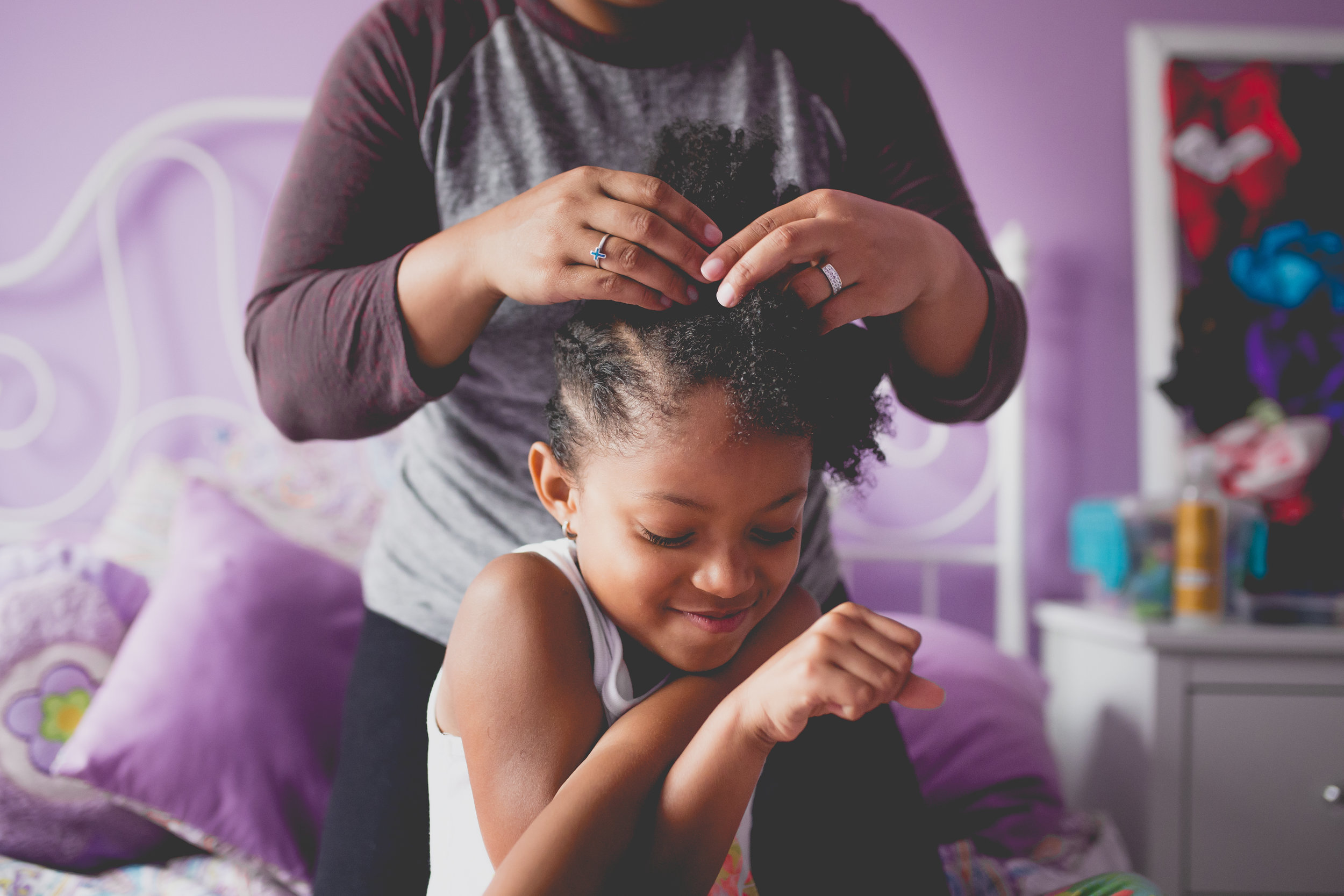 Daughter smiles while Mom puts cornrows in her hair