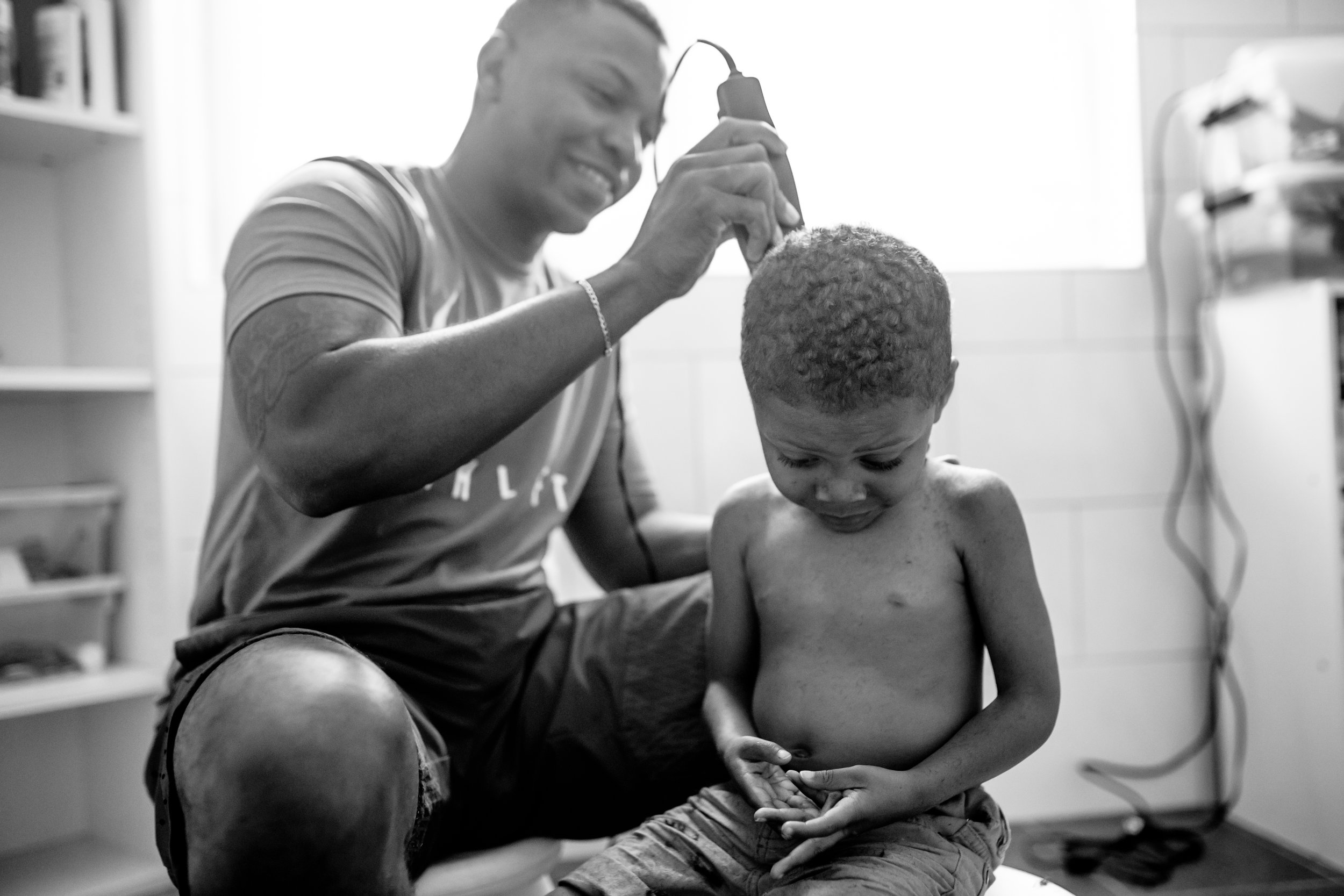 Dad smiles and cuts back of son's hair
