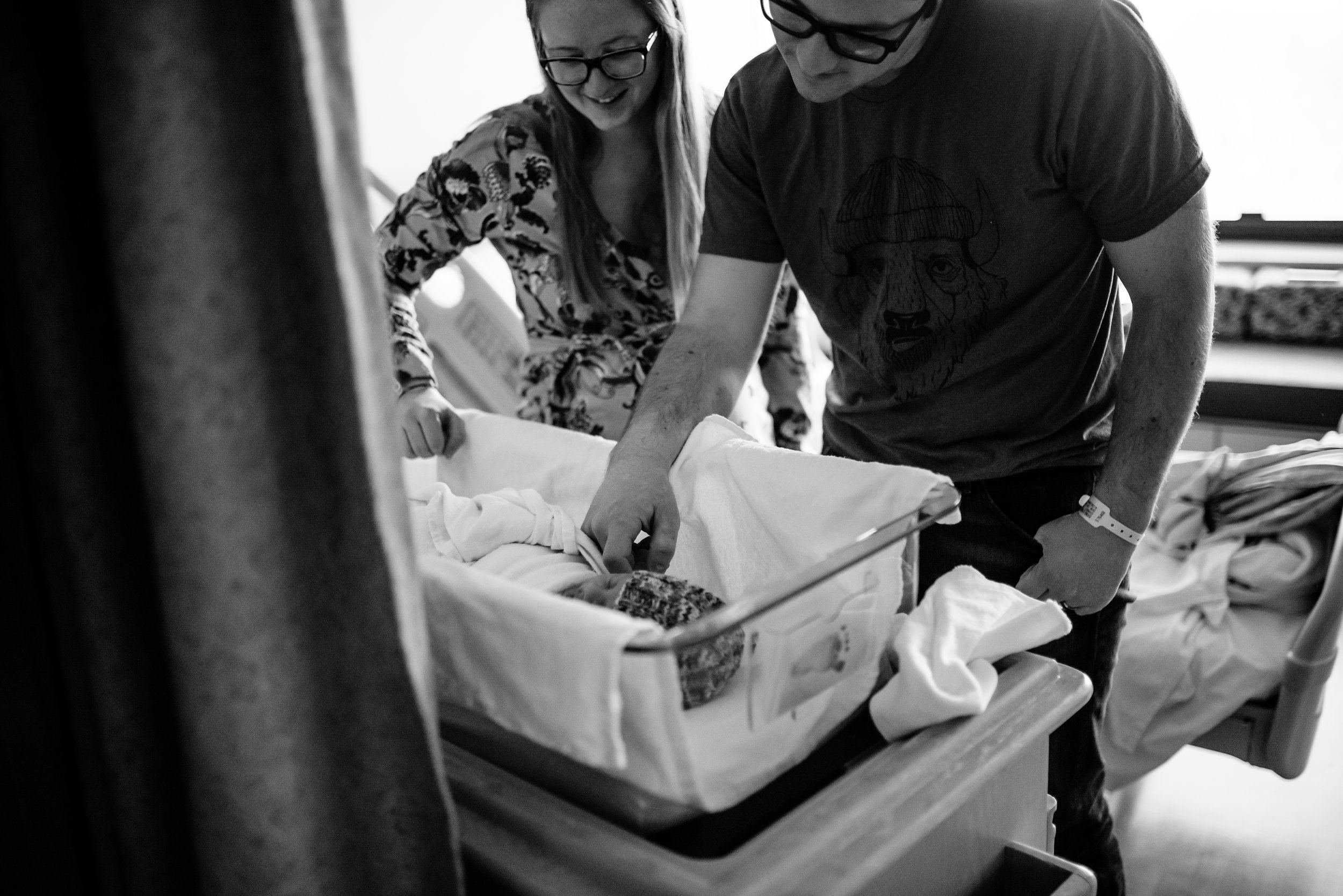 Mom and Dad smile at newborn son in hospital bassinet