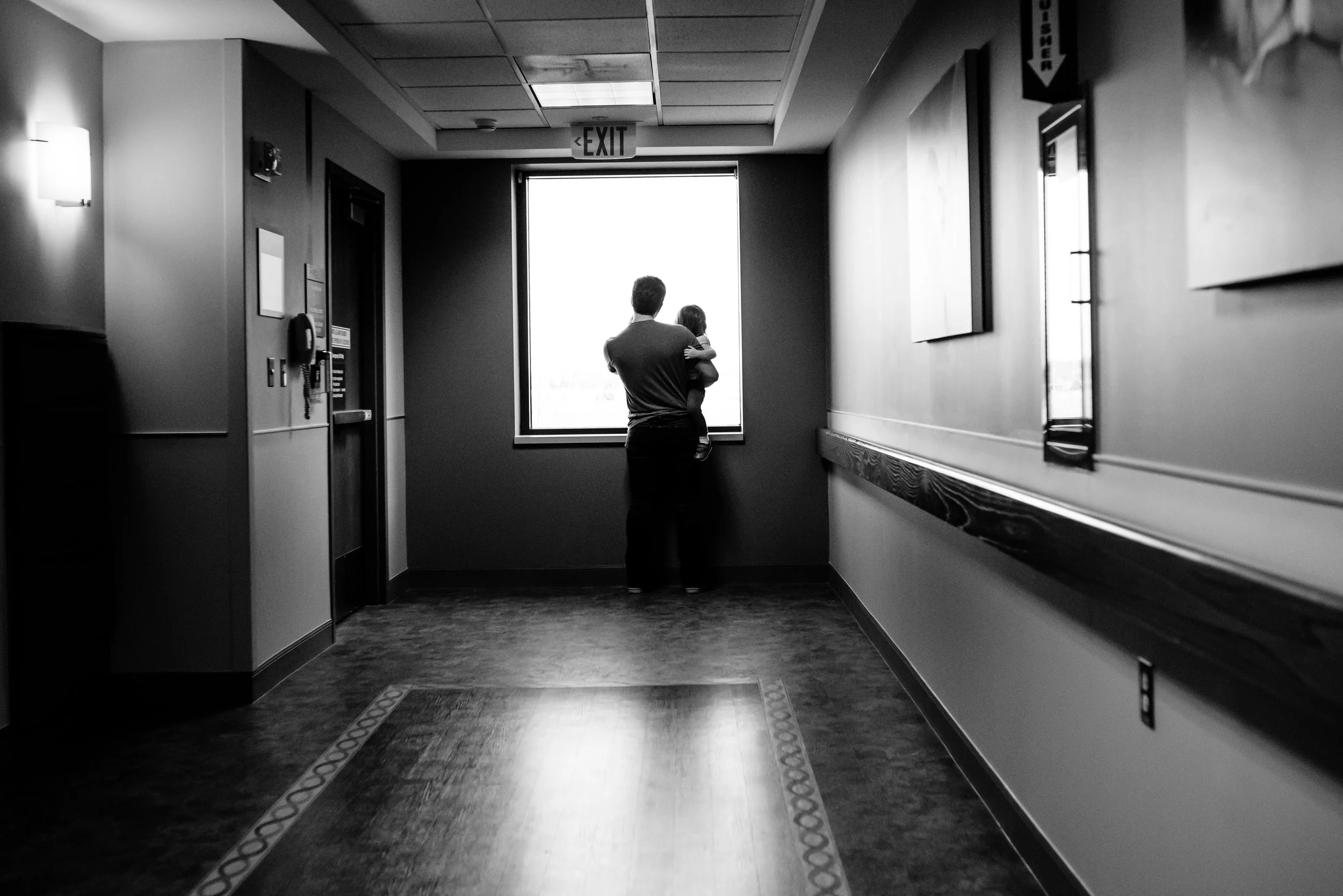 Dad holds daughter and they look outside of hospital window