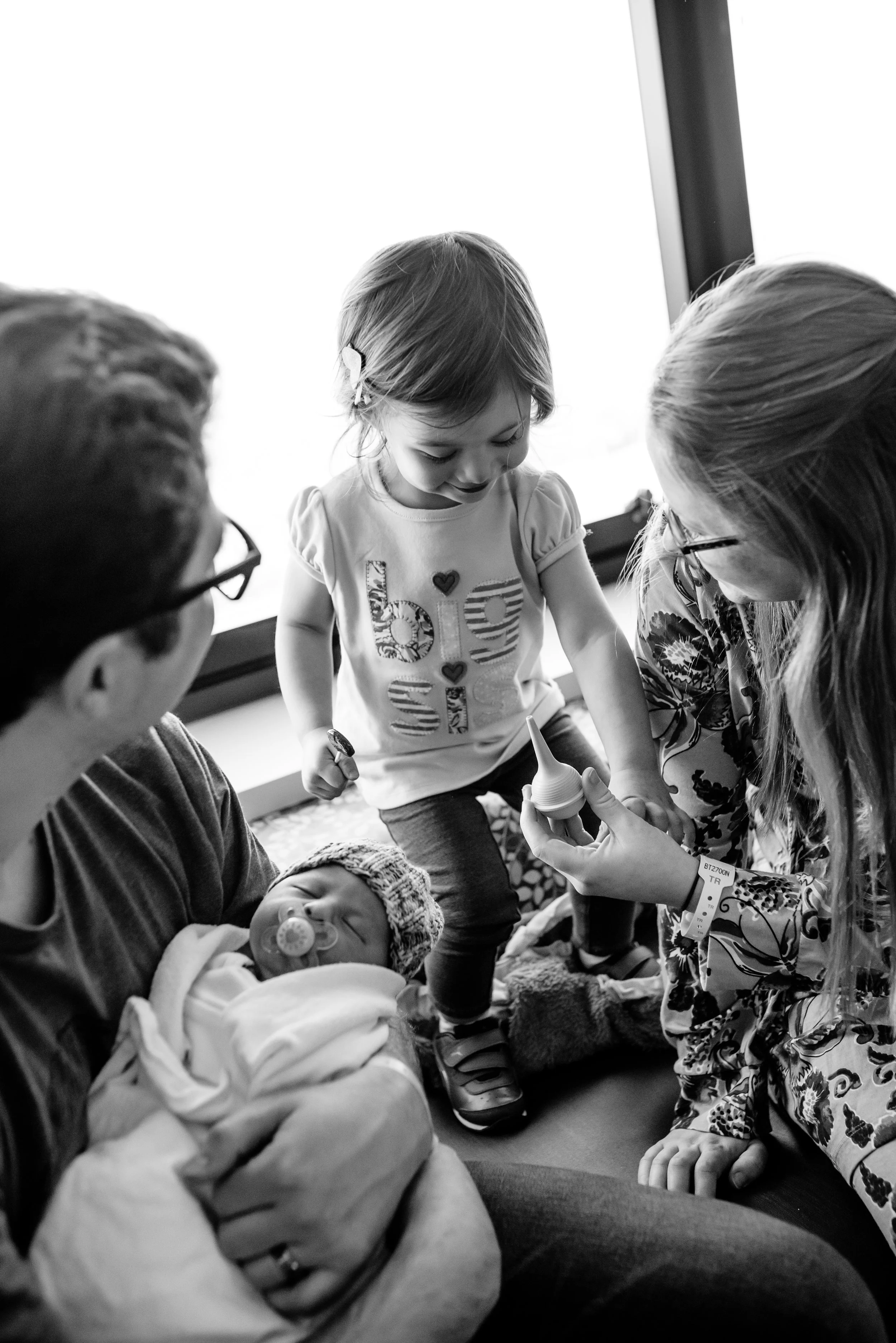 Girl smiles at nose suction with newborn brother and parents